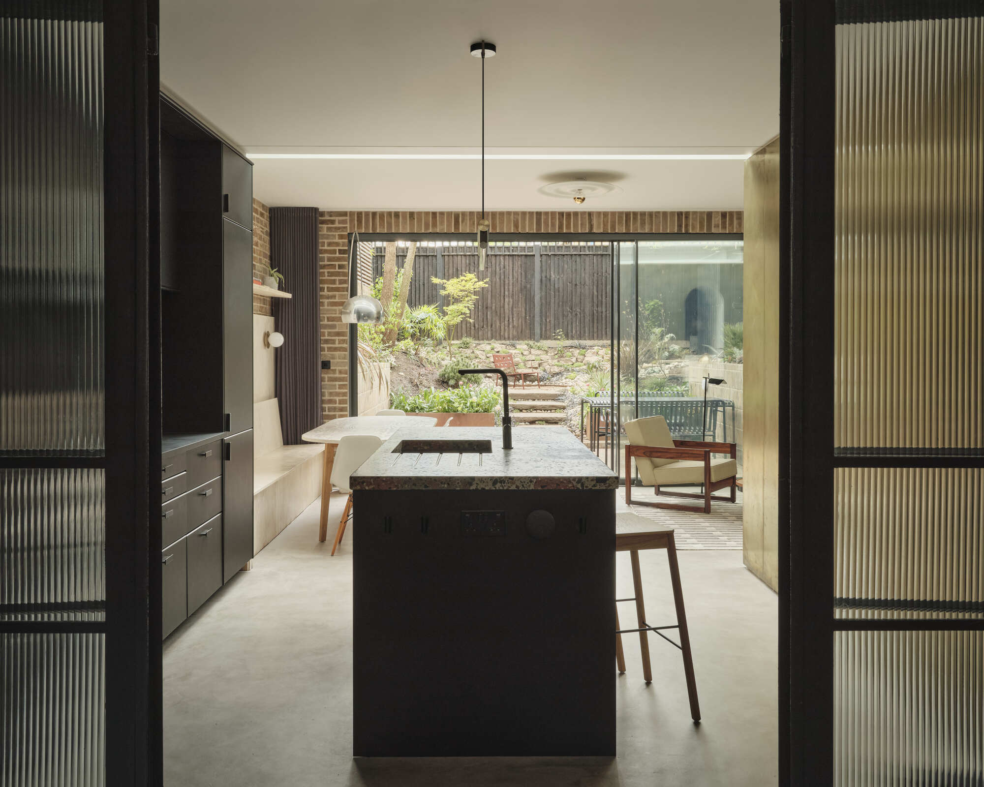 View through fluted glass doors toward kitchen island and planted rear courtyard beyond