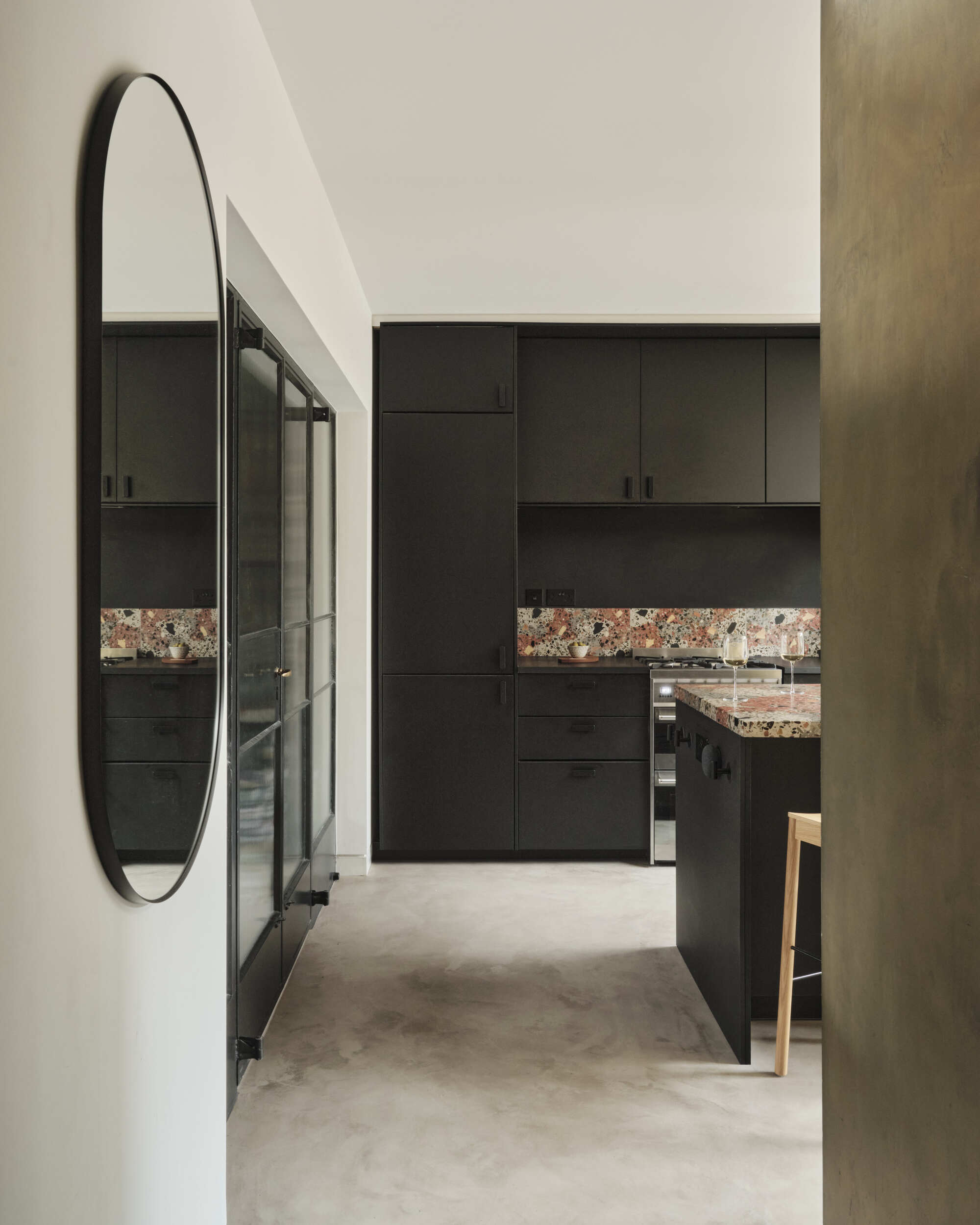 Hallway view showing oval mirror and dark joinery with multicoloured terrazzo splashback