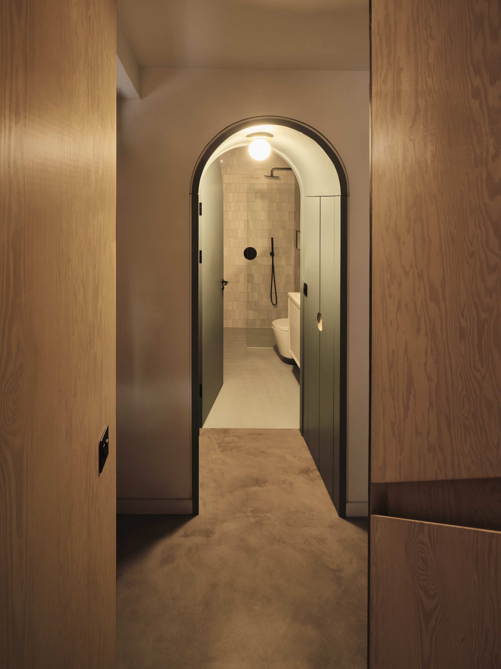 Arched doorway with black frame opening into bathroom with cream tiled walls