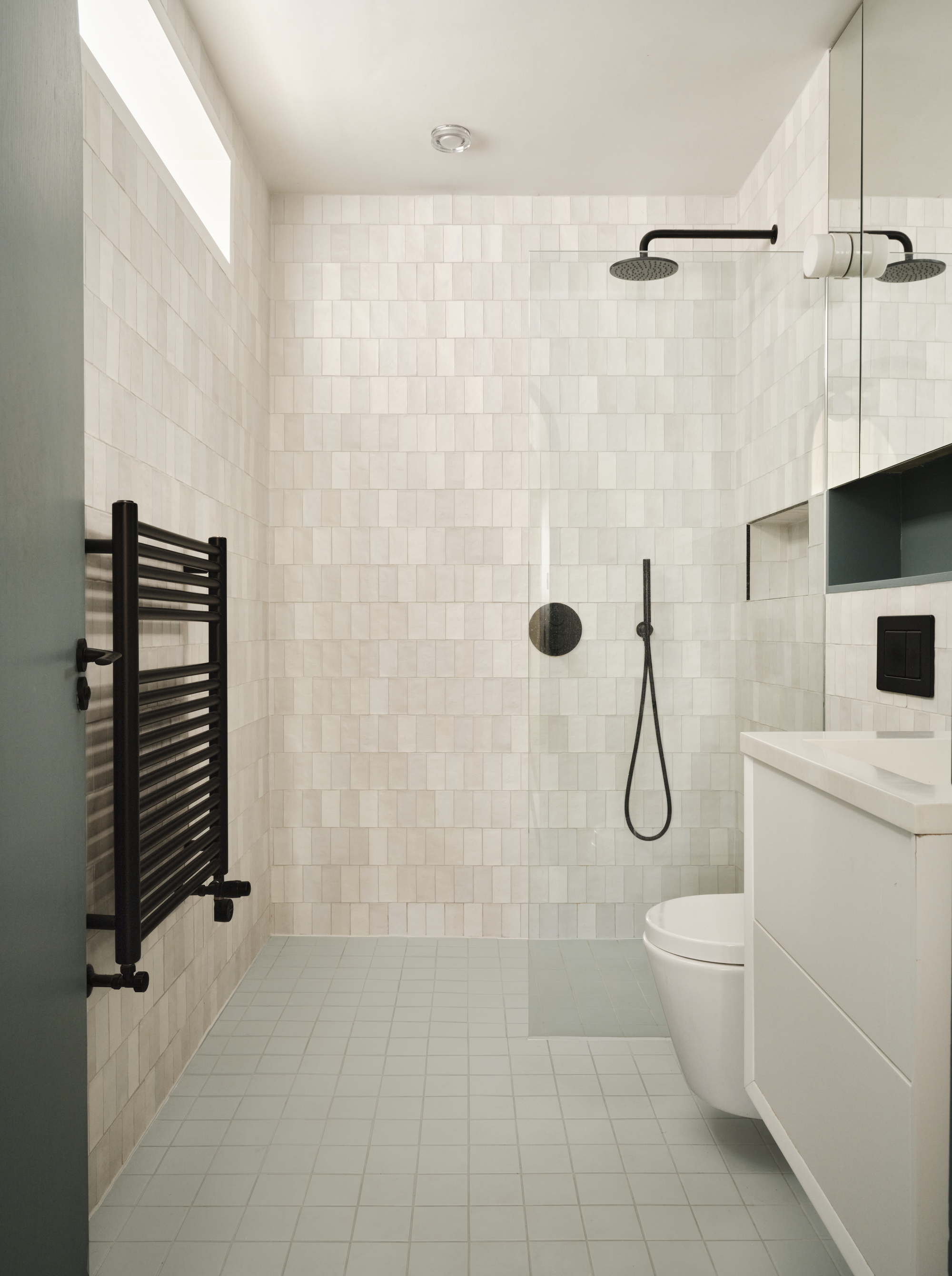 Bathroom with white square tile walls, black fixtures, towel radiator and skylight above shower area