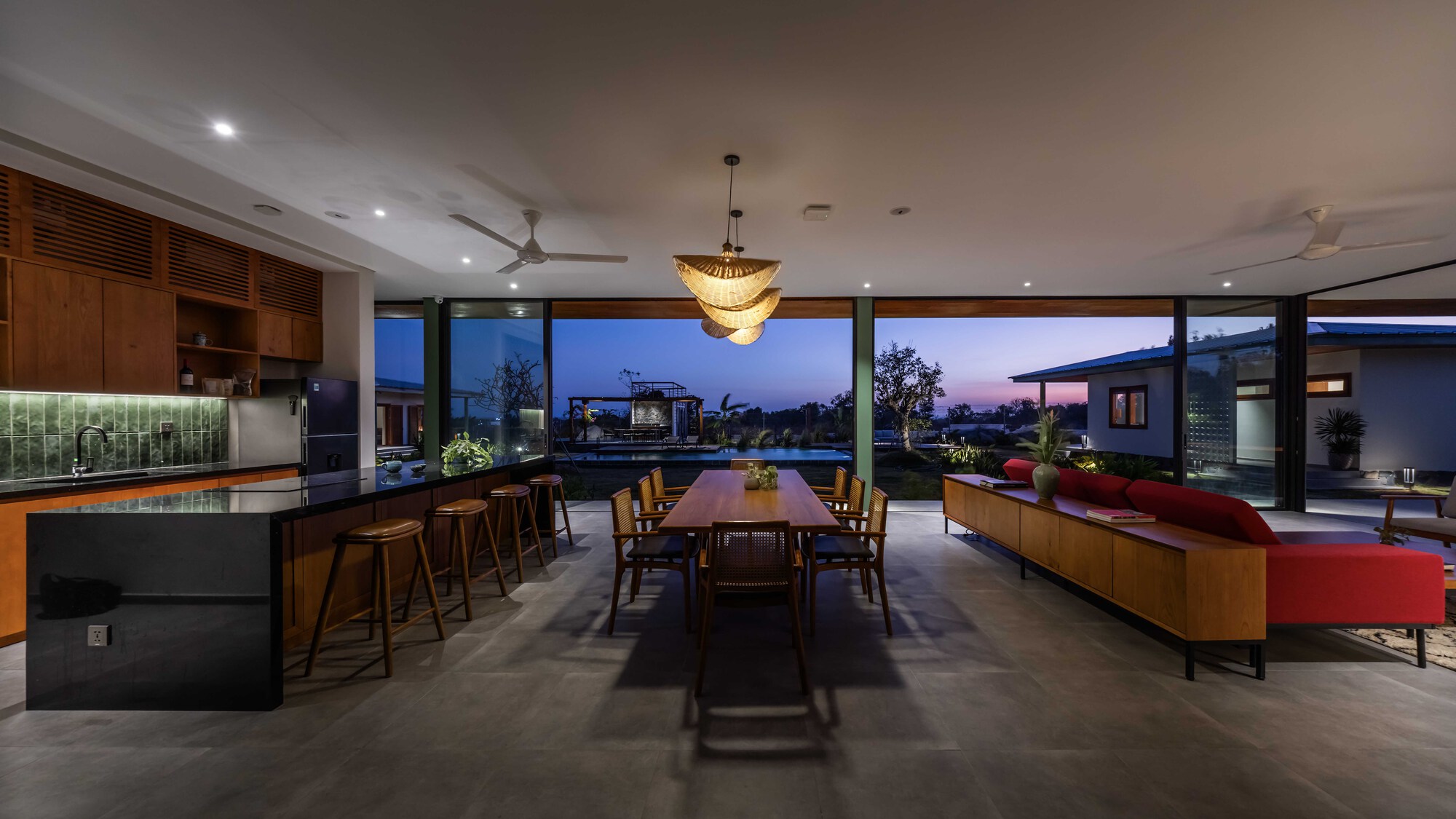 Open-plan kitchen, dining and living space with full-height glazing overlooking garden at dusk