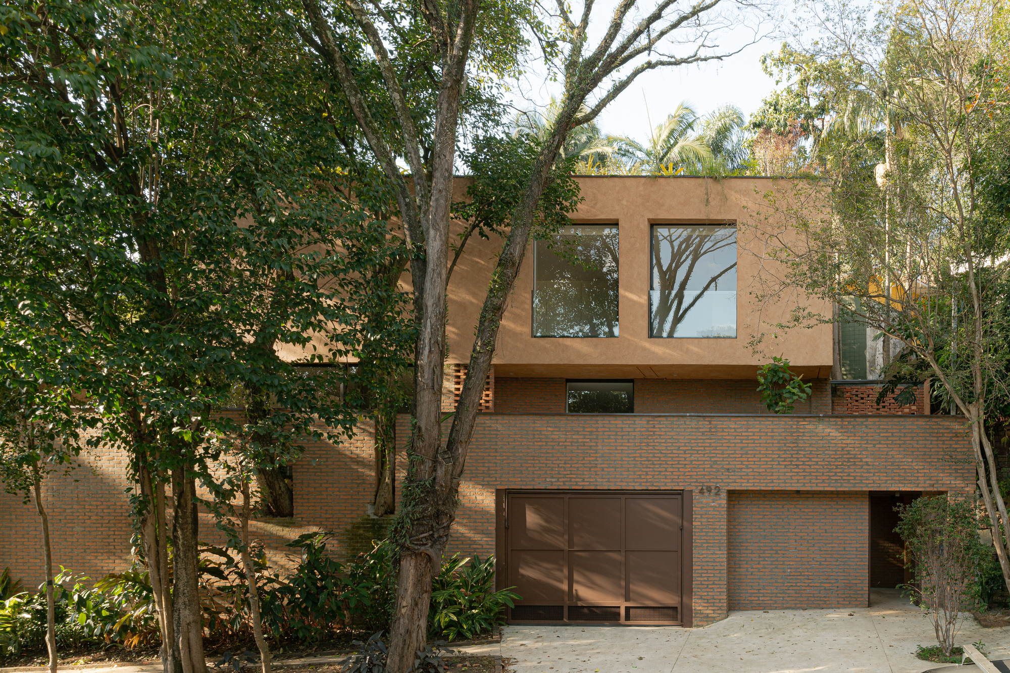 Street facade with brick base and timber-clad upper volume framed by mature trees