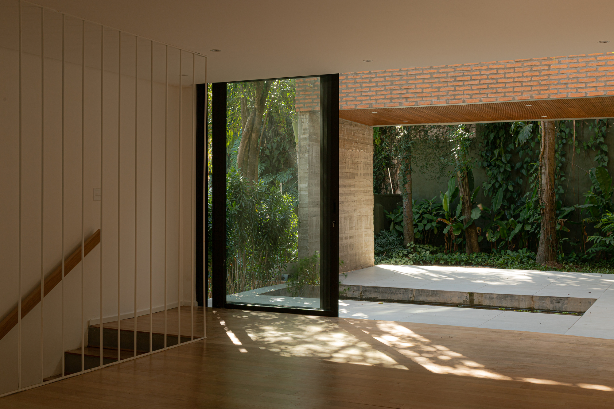 Timber staircase alongside full-height glazing opening to a sunlit patio with exposed brick ceiling