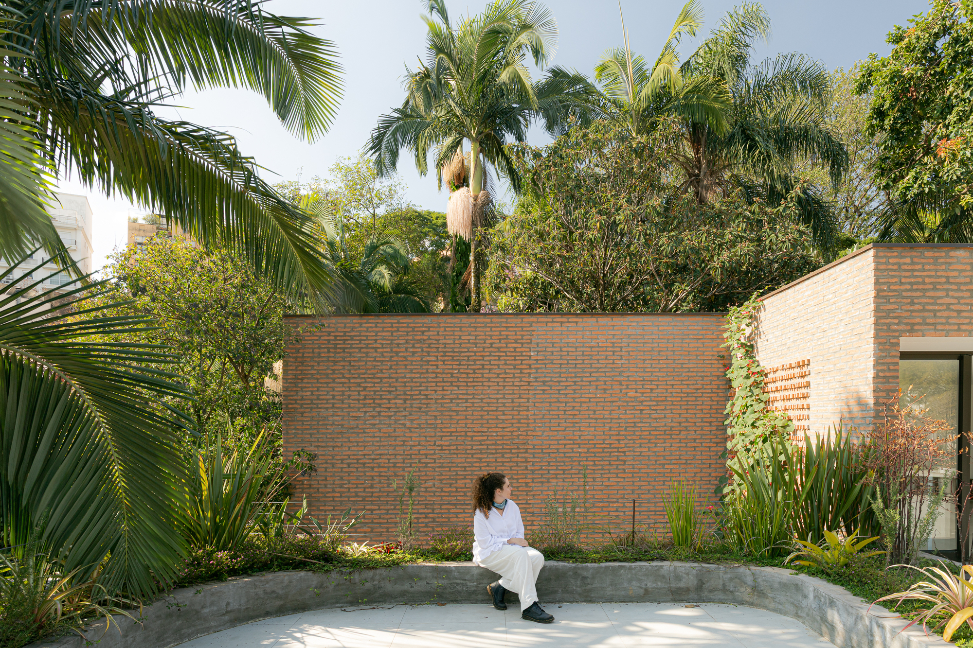 Concrete bench in courtyard surrounded by brick wall and tropical palms with seated figure