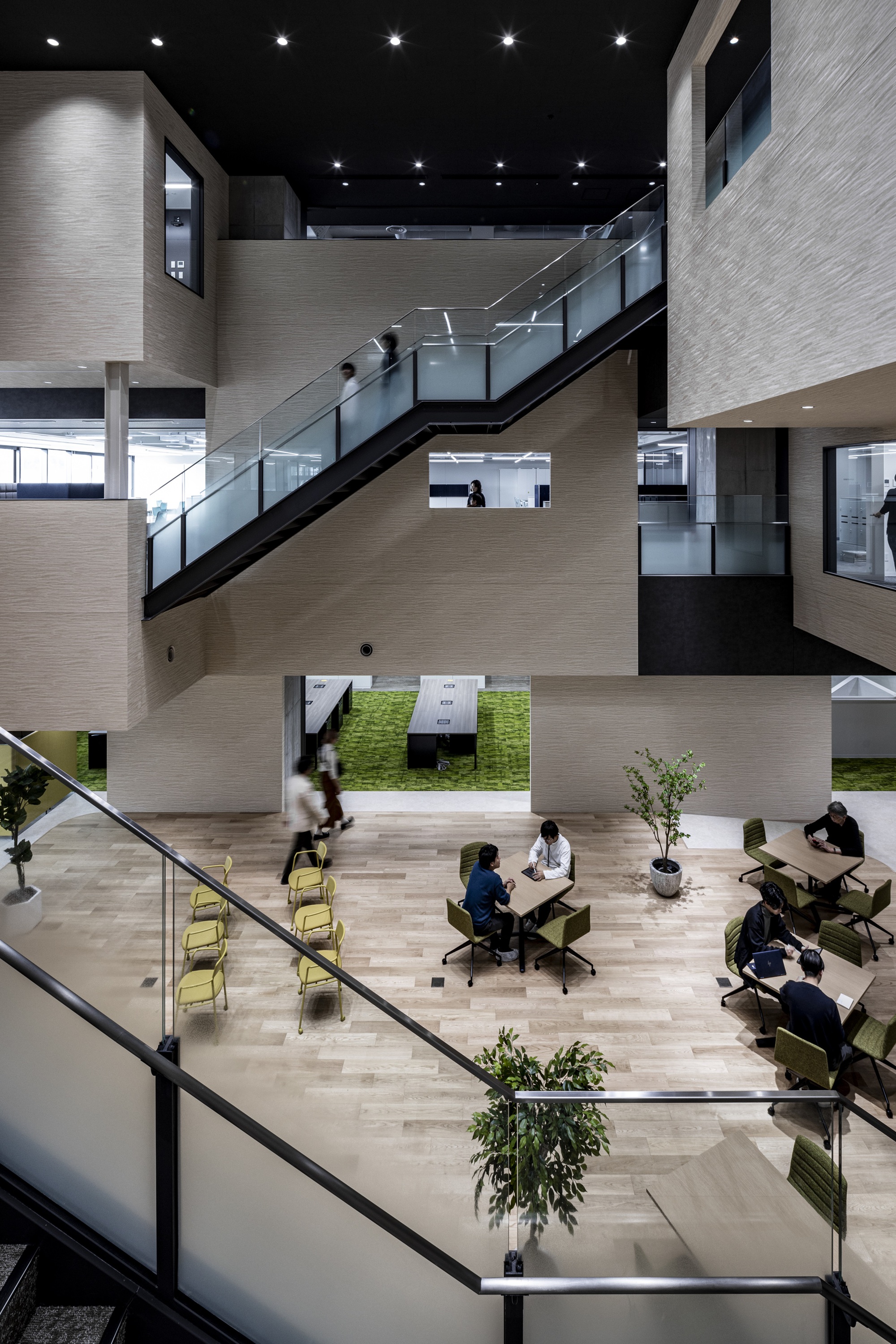 Atrium interior with metal-and-glass staircases linking floors, people seated at tables and a grass-covered courtyard below