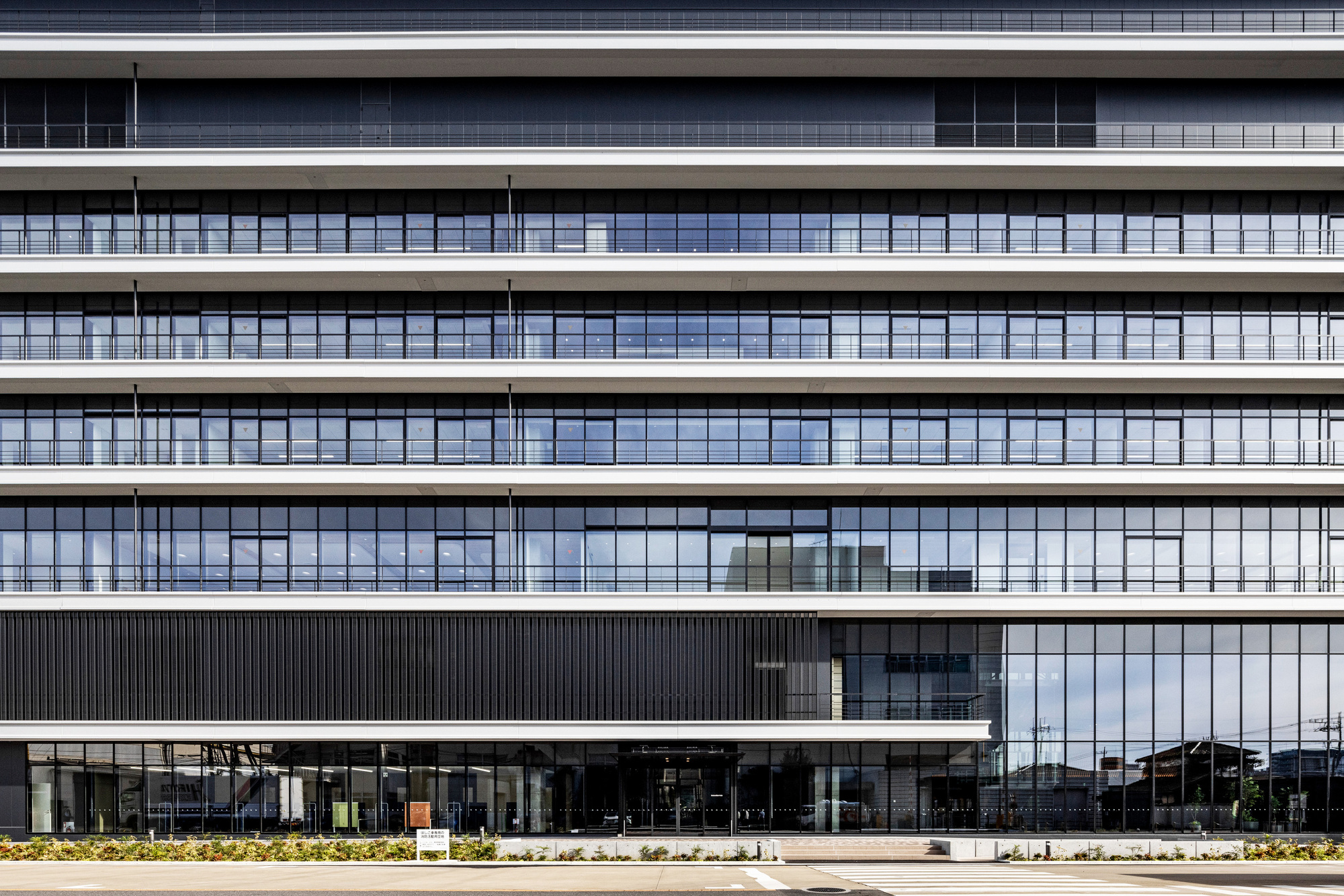 Facade showing horizontal bands of glazing with slender vertical mullions above a planted ground level