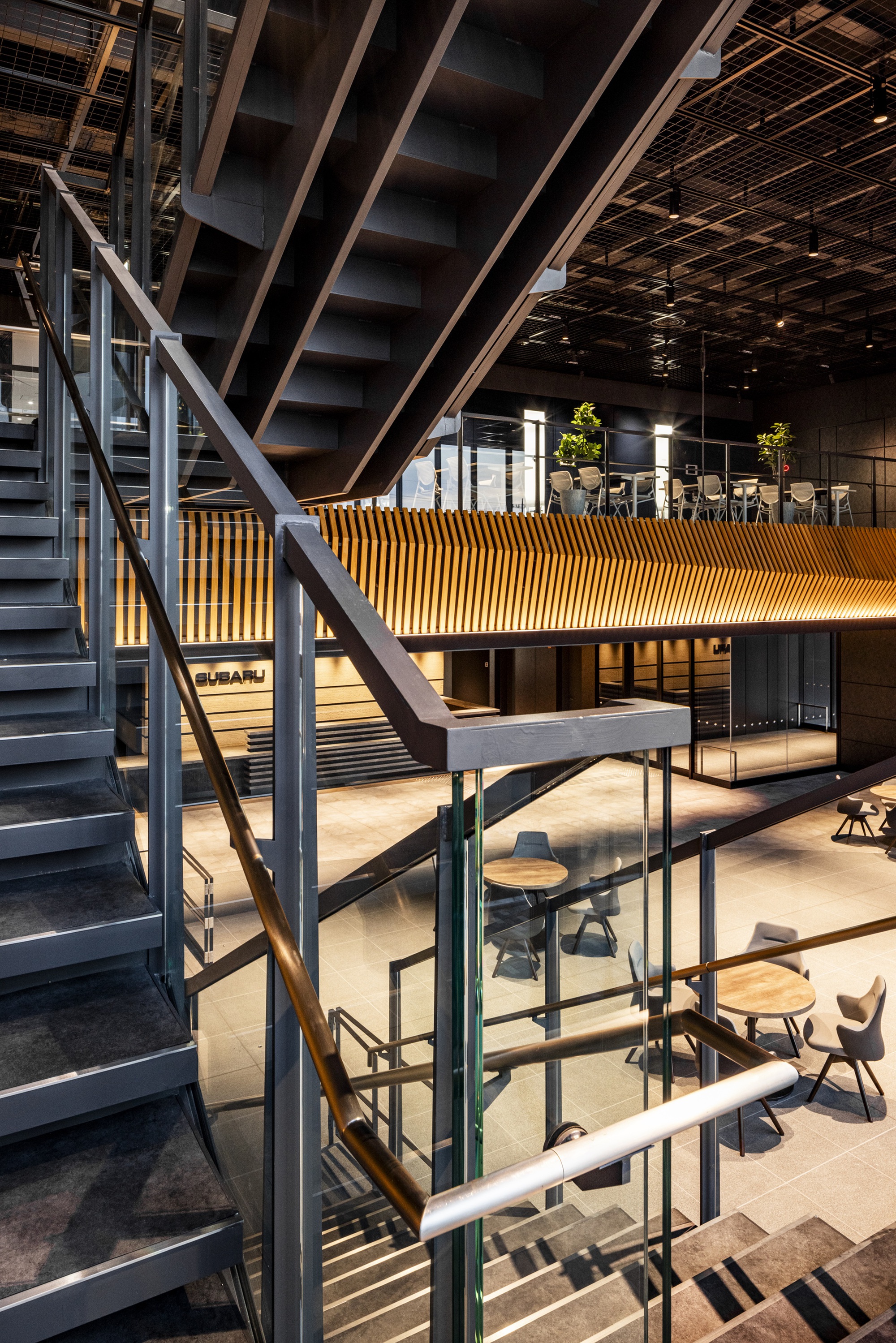 Vertical view of interconnected steel stairs, glass railings, and timber slatted bridge spanning between levels