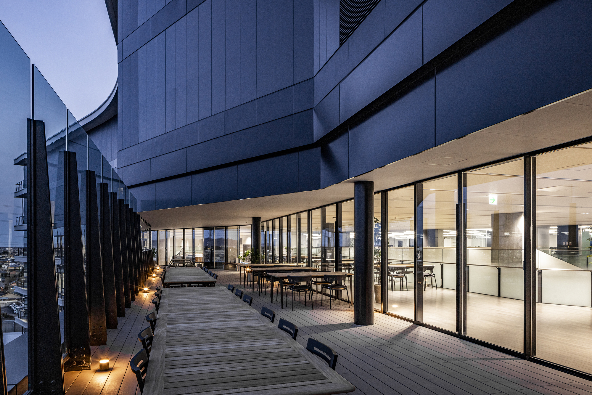 Timber deck terrace with glass-walled dining space and vertical metal fins at dusk