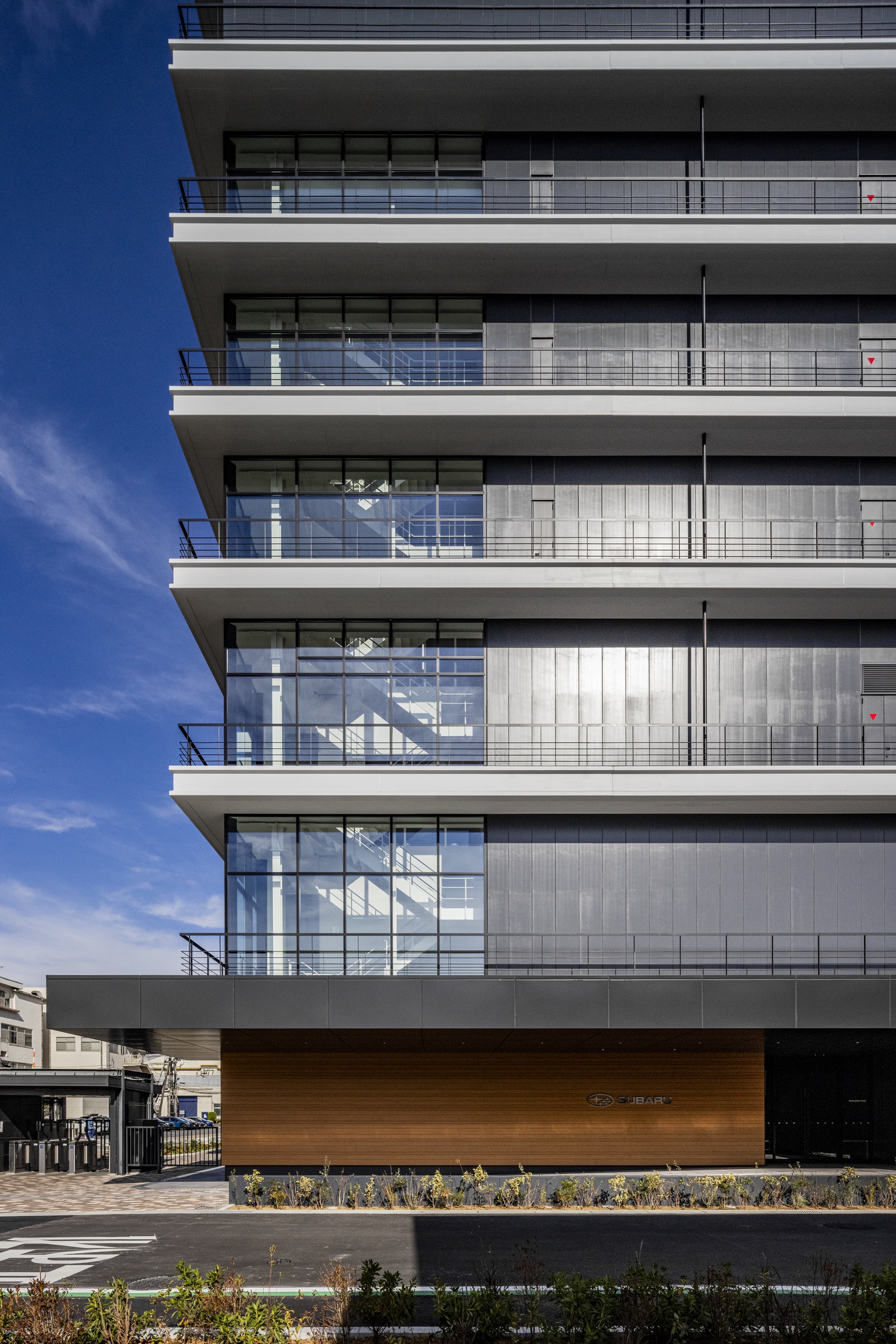 Stacked balconies with glass and solid cladding above a timber-clad base and planted bed