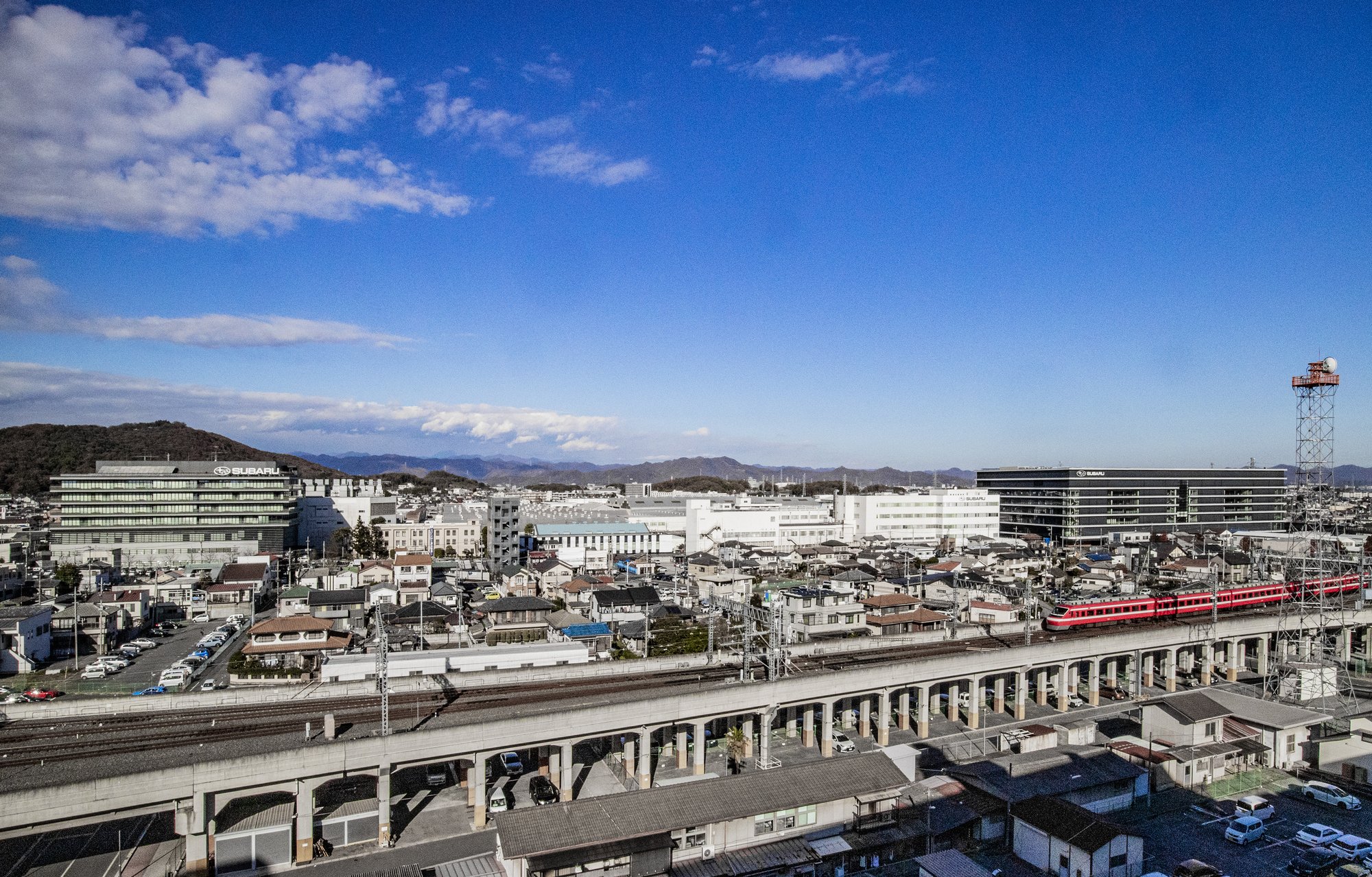 Elevated view across rail lines and residential rooftops toward the horizontal banded volumes
