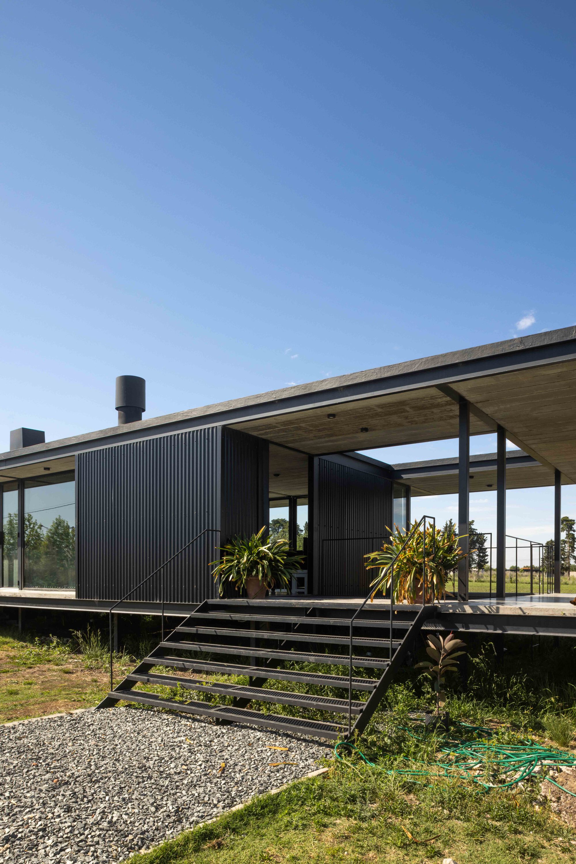 Steel staircase leading to timber-ceilinged deck with corrugated cladding and potted palms