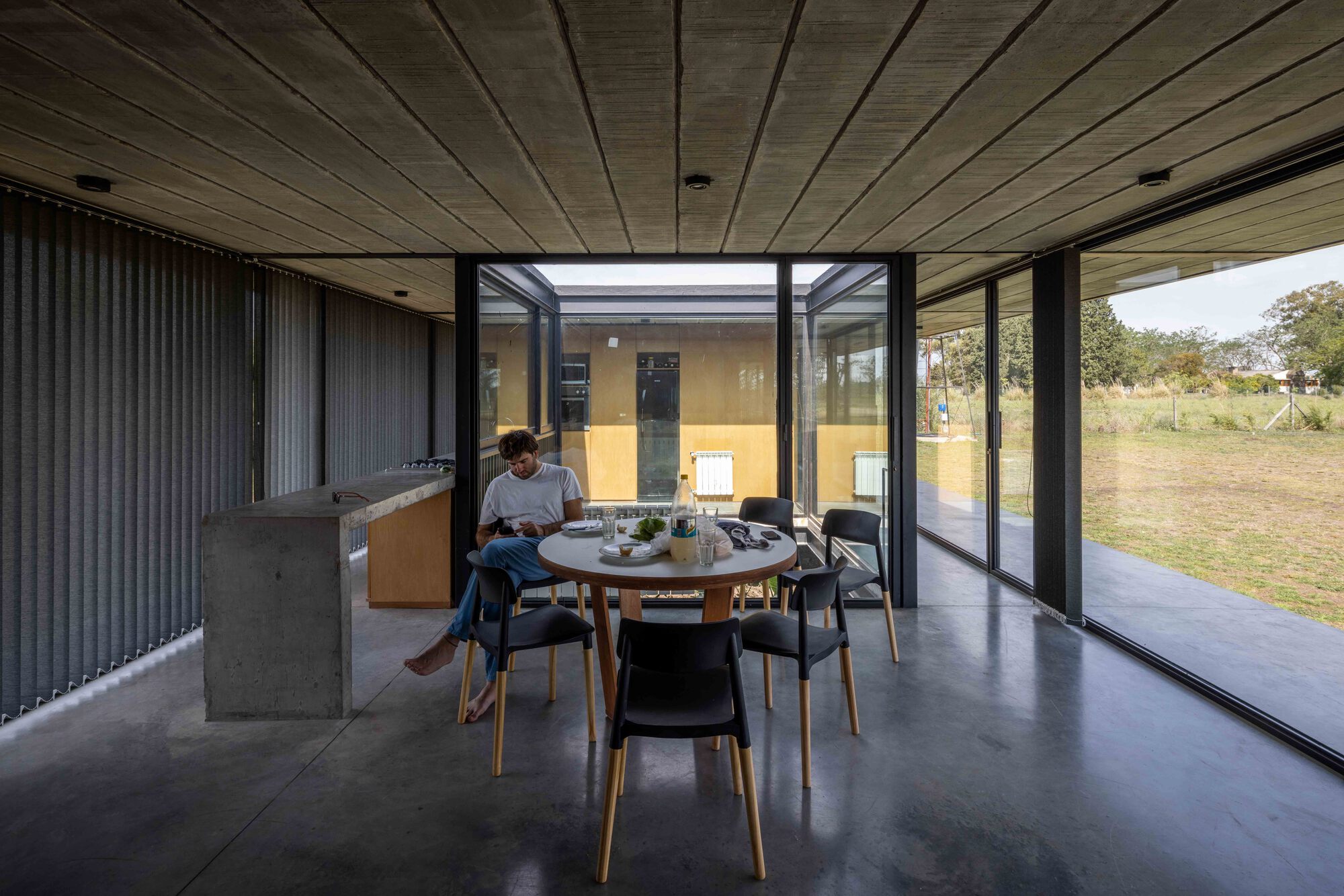 Dining area with concrete floor and timber ceiling opening to landscape through floor-to-ceiling glass