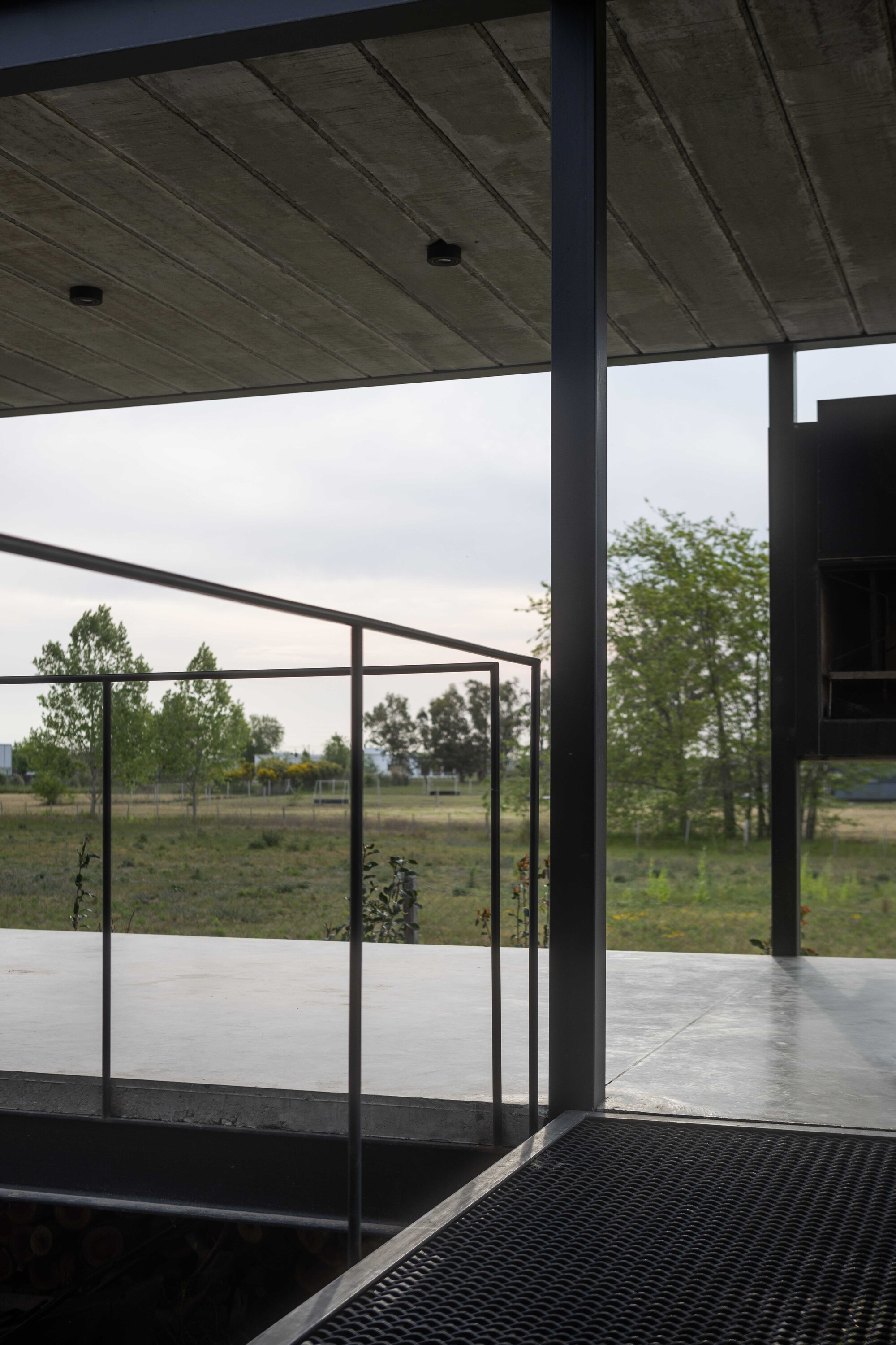 View through steel-framed glass door opening onto covered terrace under overcast sky