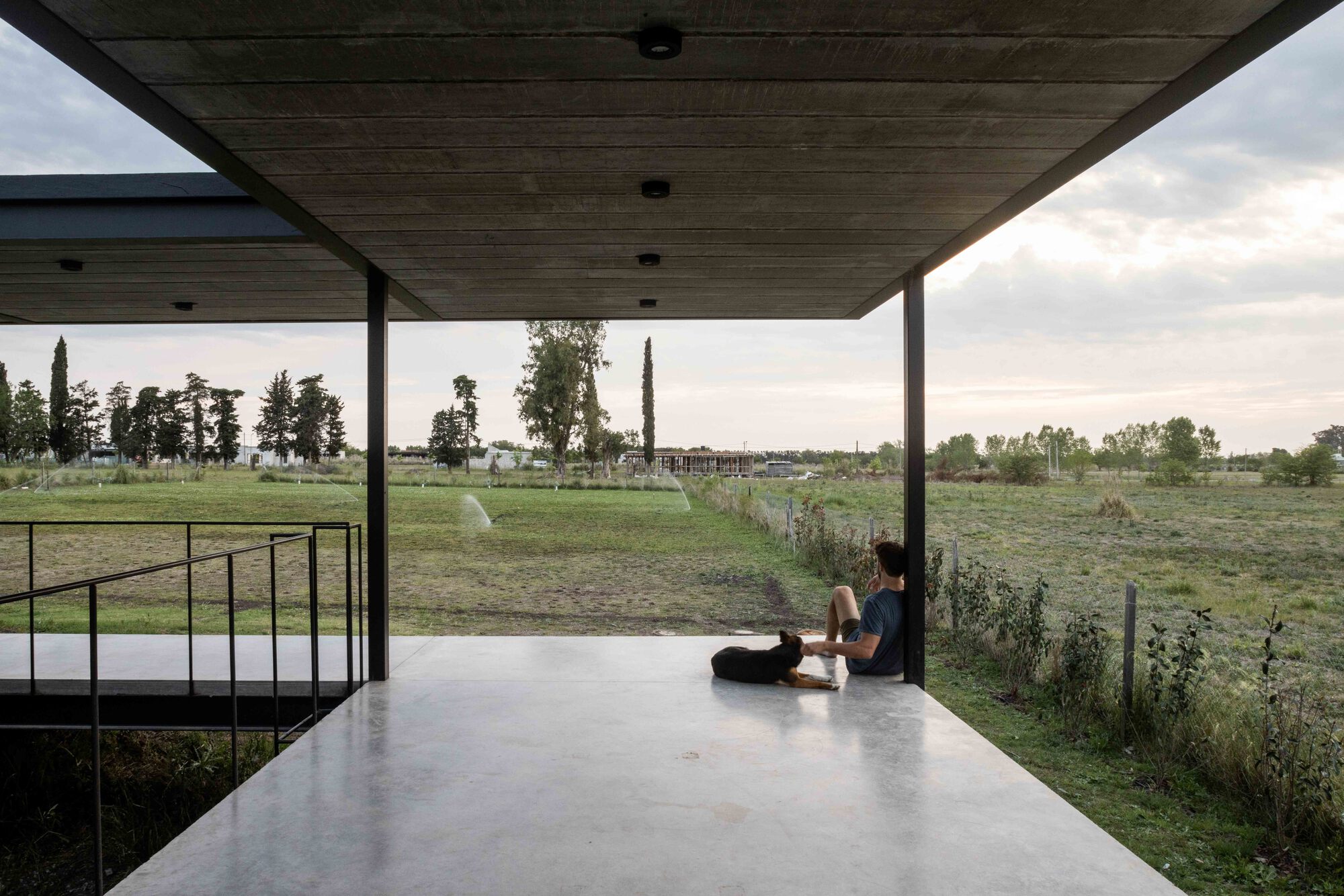Covered terrace with timber ceiling where two figures sit on polished concrete floor overlooking fields