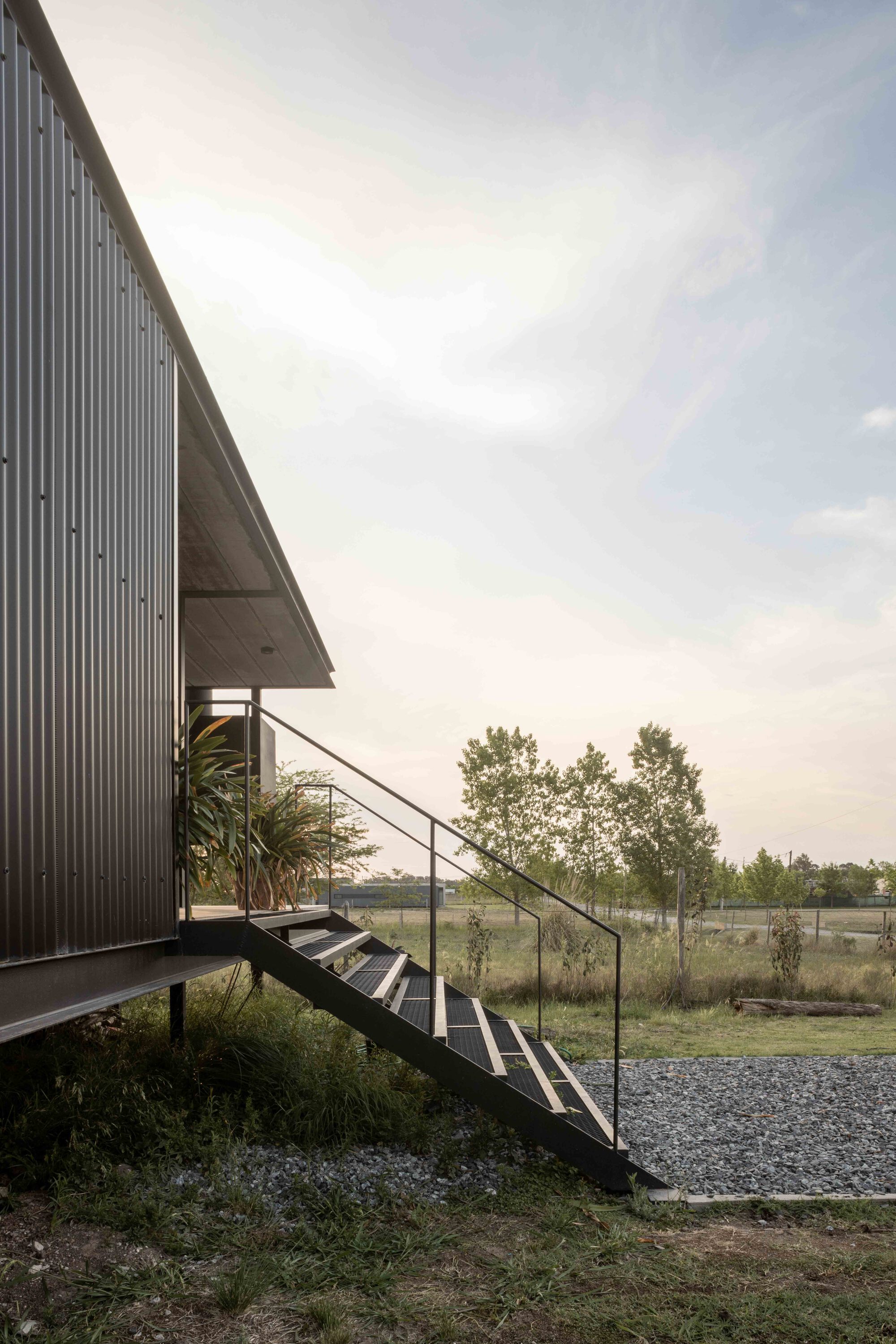 Steel staircase with glass railings ascending to the corrugated metal facade under overcast sky
