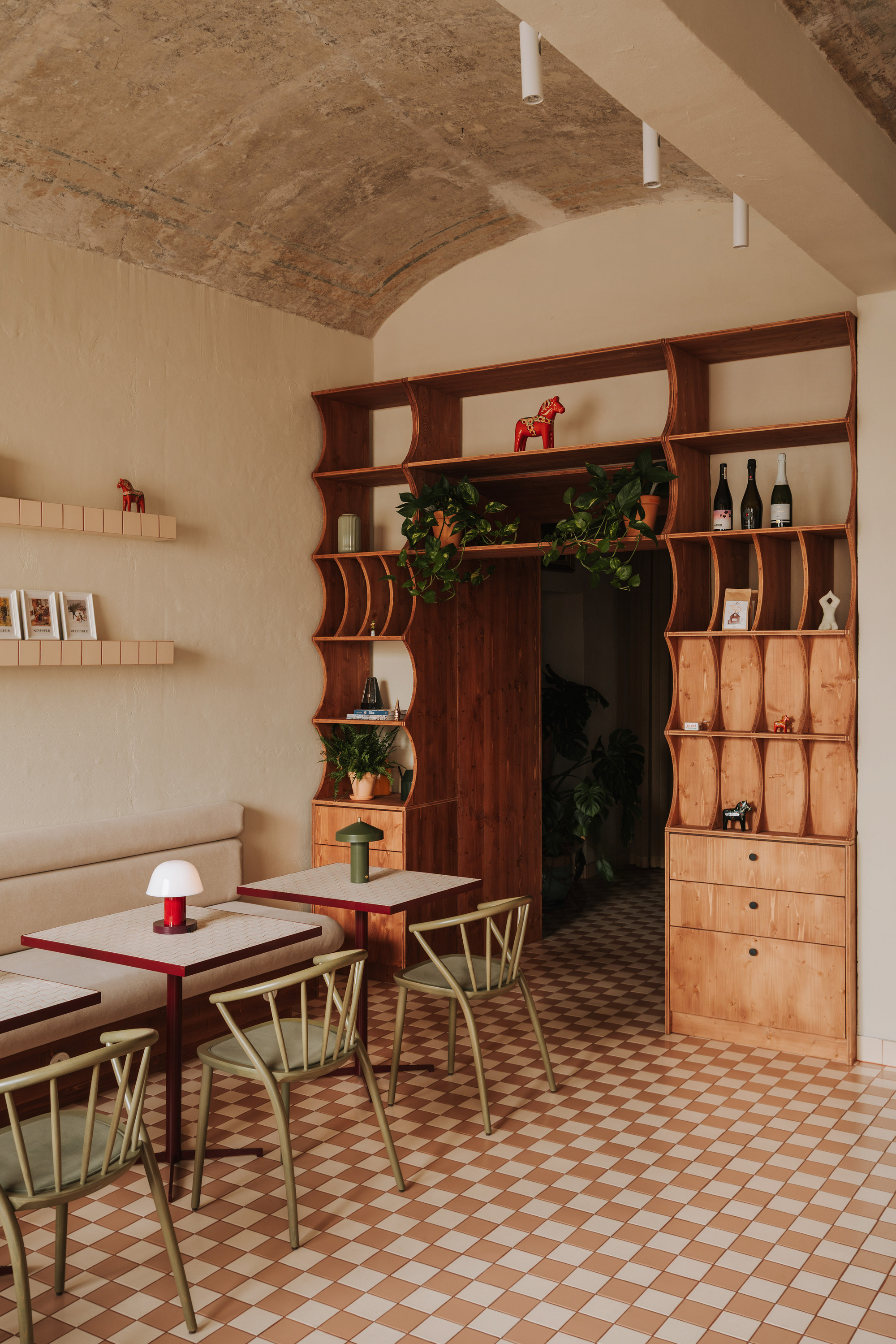 Curved timber shelving unit with integrated doorway under an exposed brick barrel vault ceiling