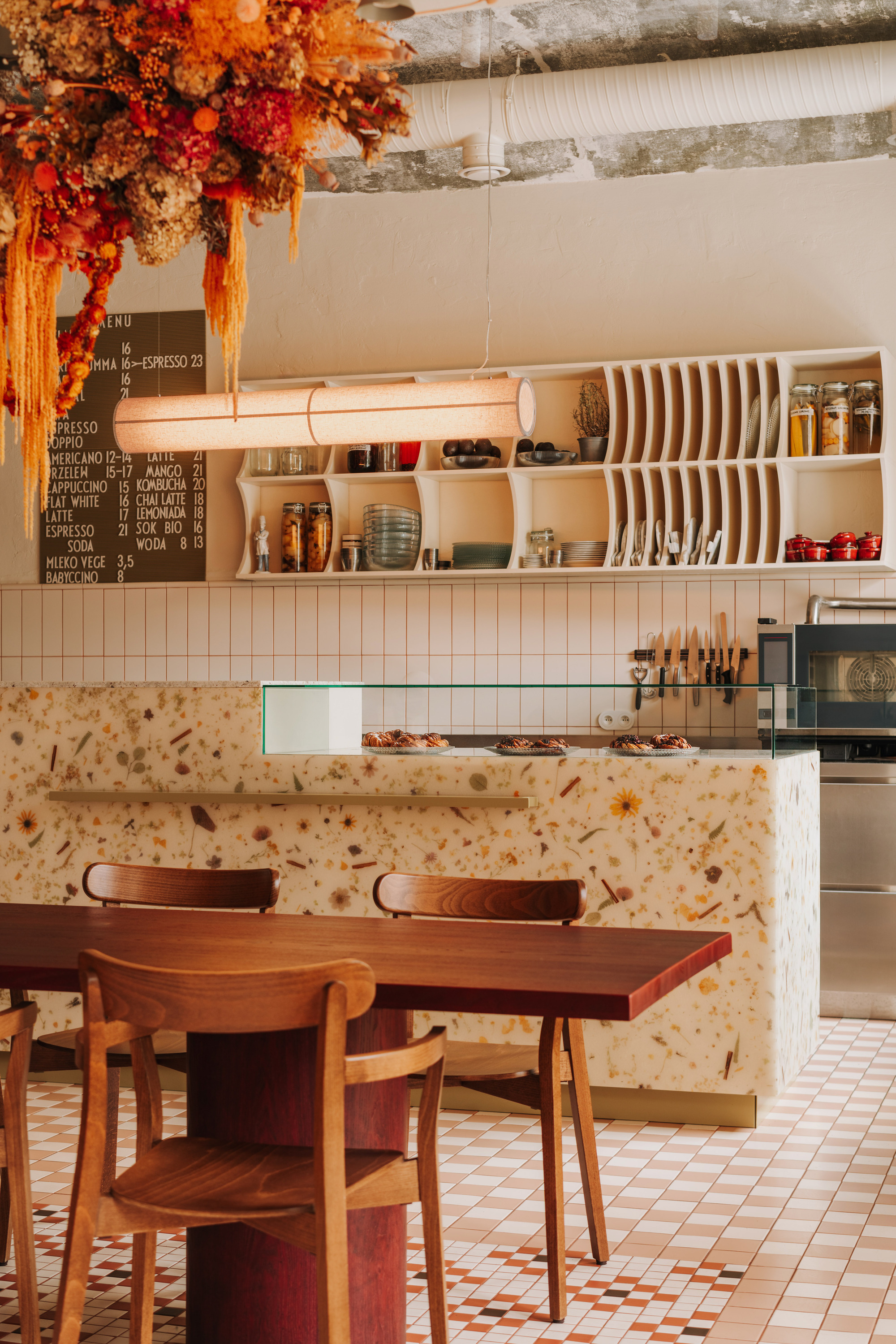 Service counter clad in terrazzo with dried flower installation hanging from the exposed ceiling joists