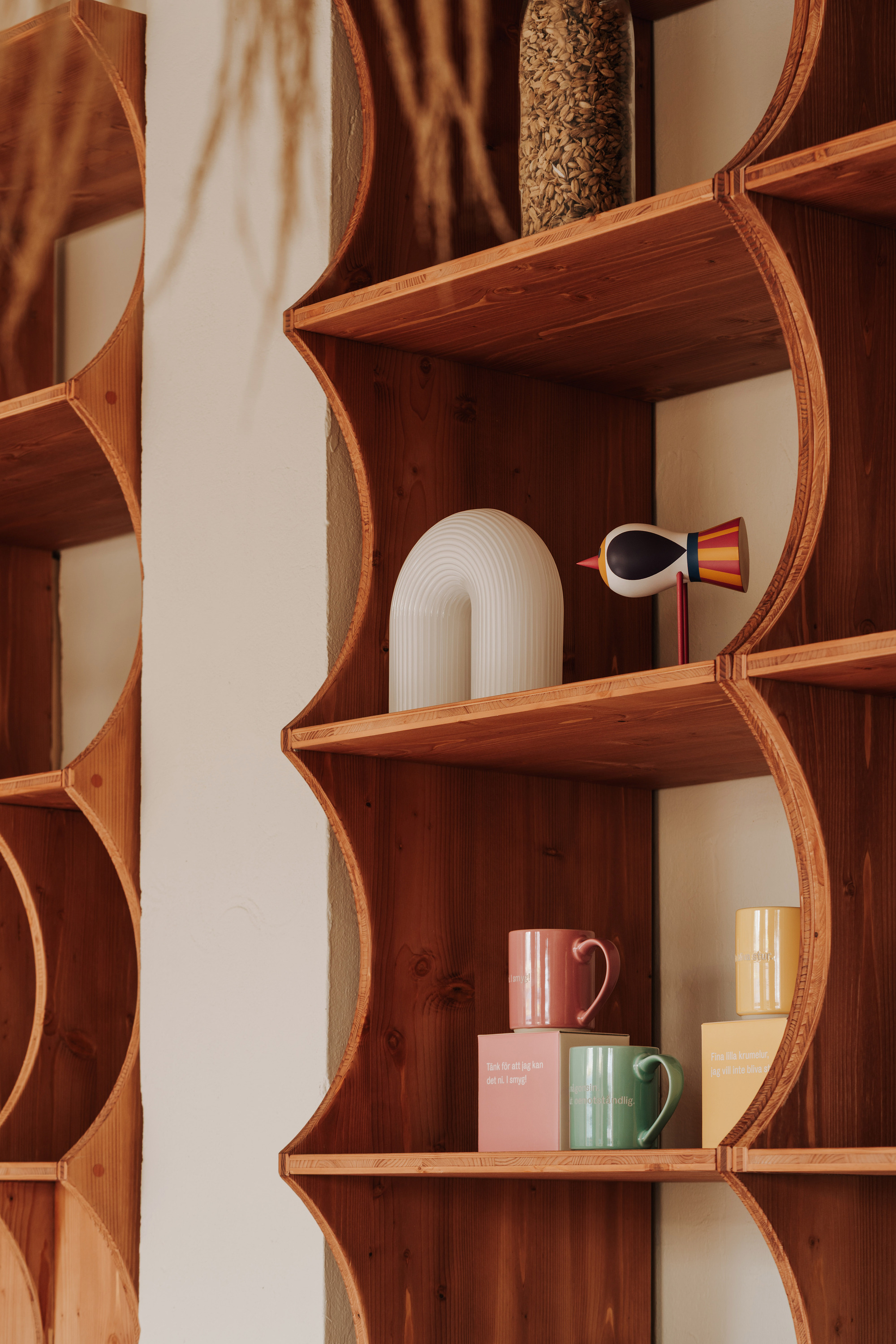 Curved timber shelving unit displaying ceramic vessels and cups in warm light