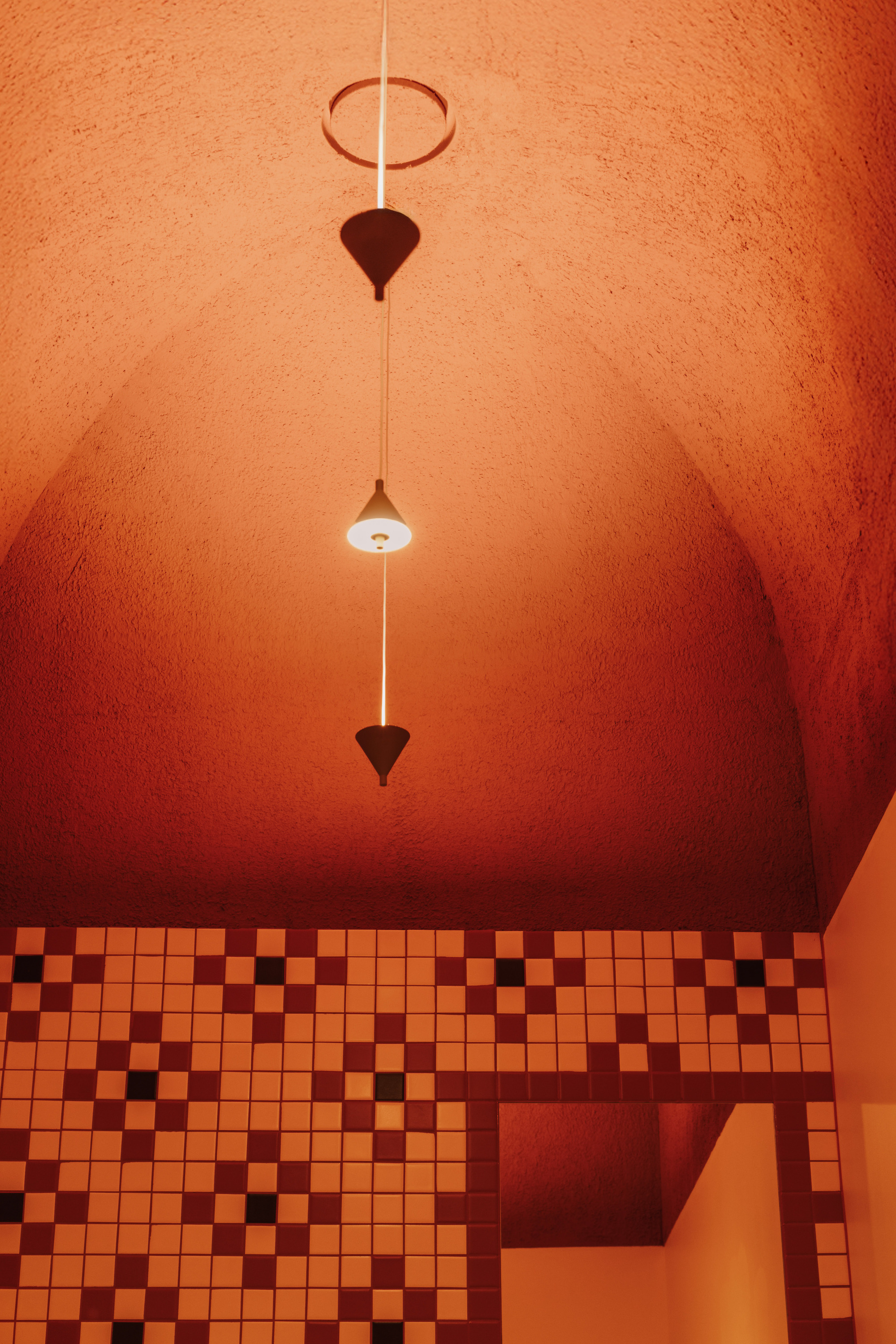 Vaulted ceiling painted terracotta orange with pendant light above chequered tile floor