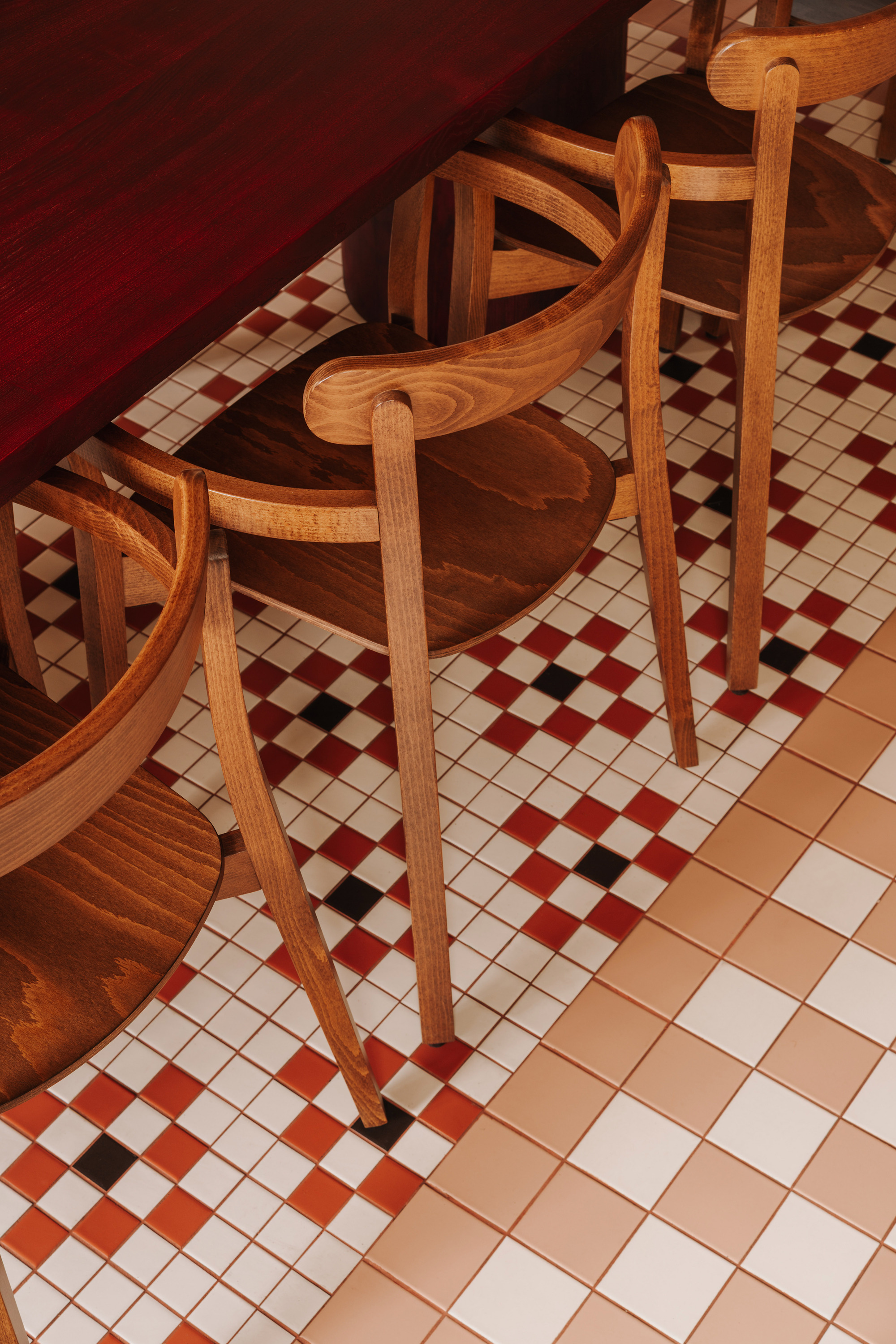 Overhead view of timber chairs arranged on diagonal chequered tile floor in warm light