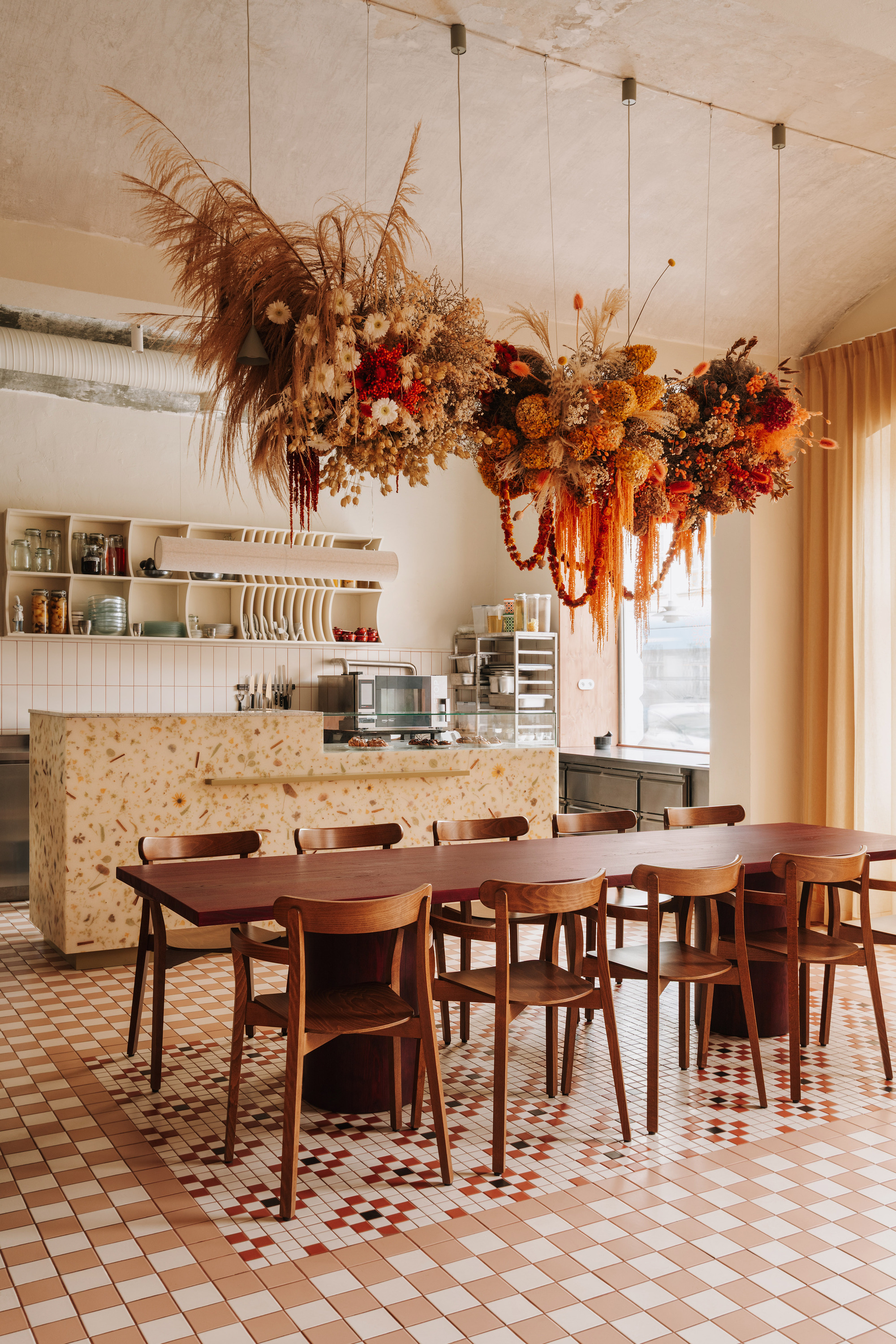 Dining room with large dried floral installation above timber table and chipboard service counter