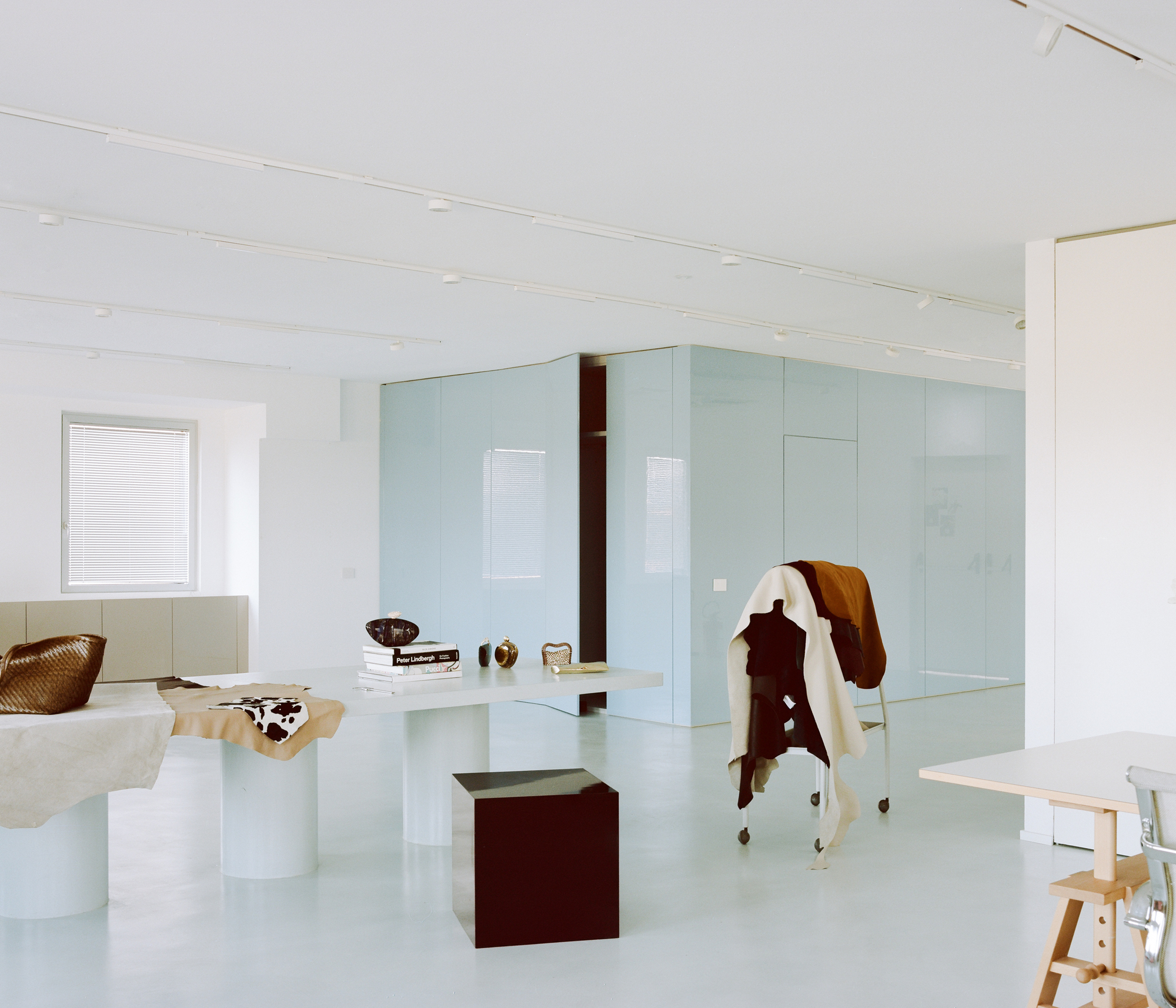 Pale blue glass partition enclosing workspace with cowhide draped over maroon cube