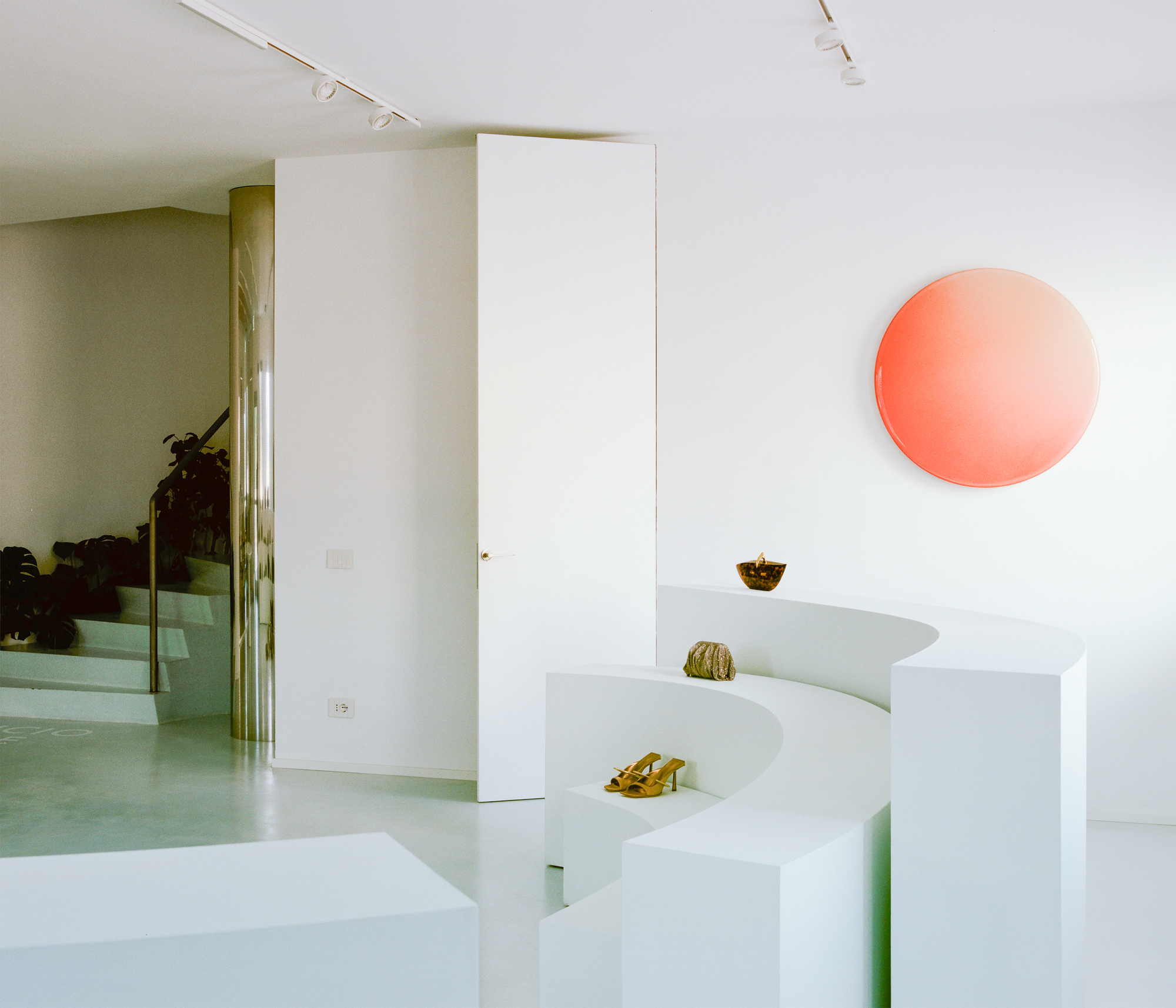 White stepped display platform with coral circular wall light above concrete floor