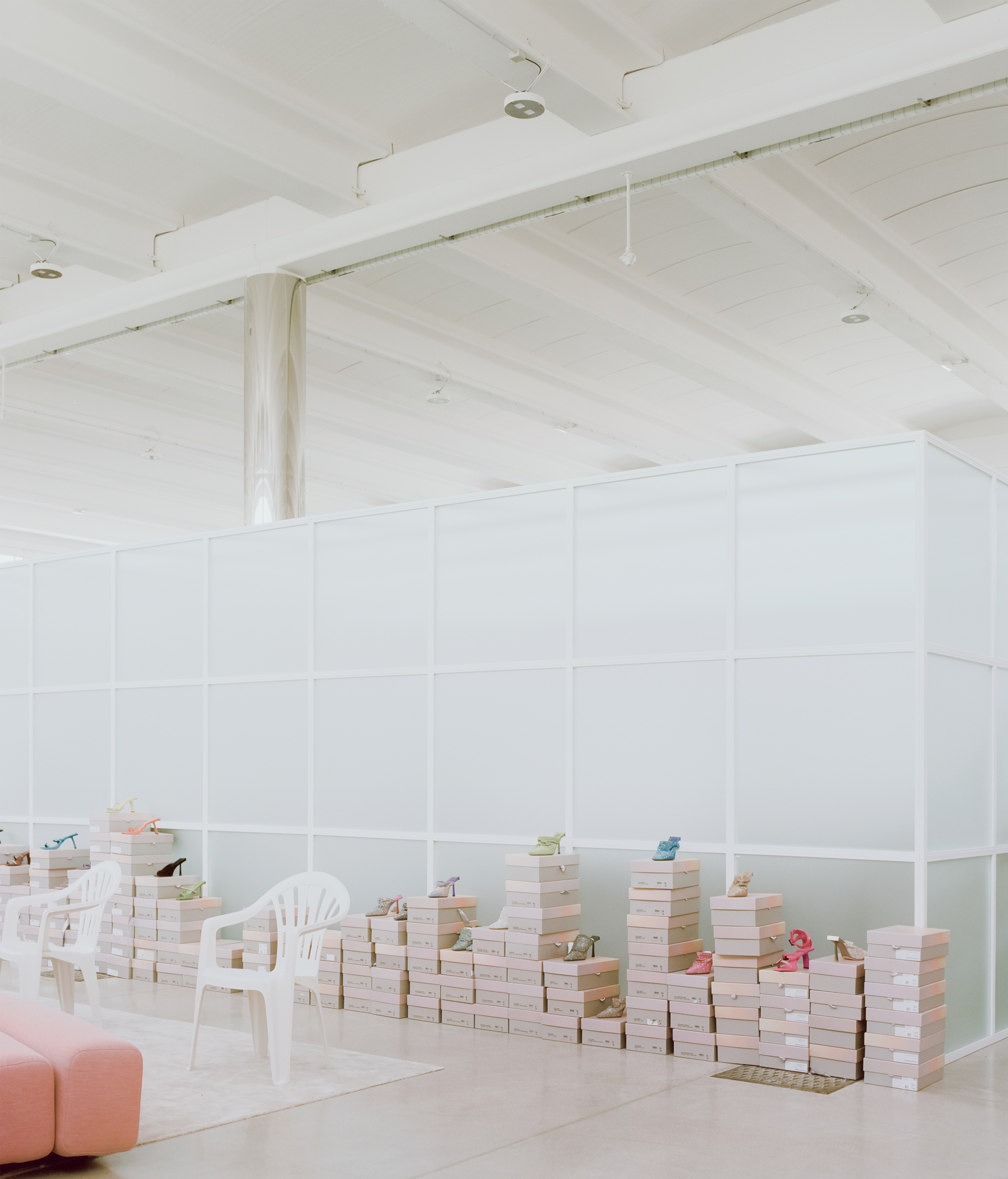 White paneled partition enclosing a room with stacked books and white plastic chairs under exposed ceiling beams