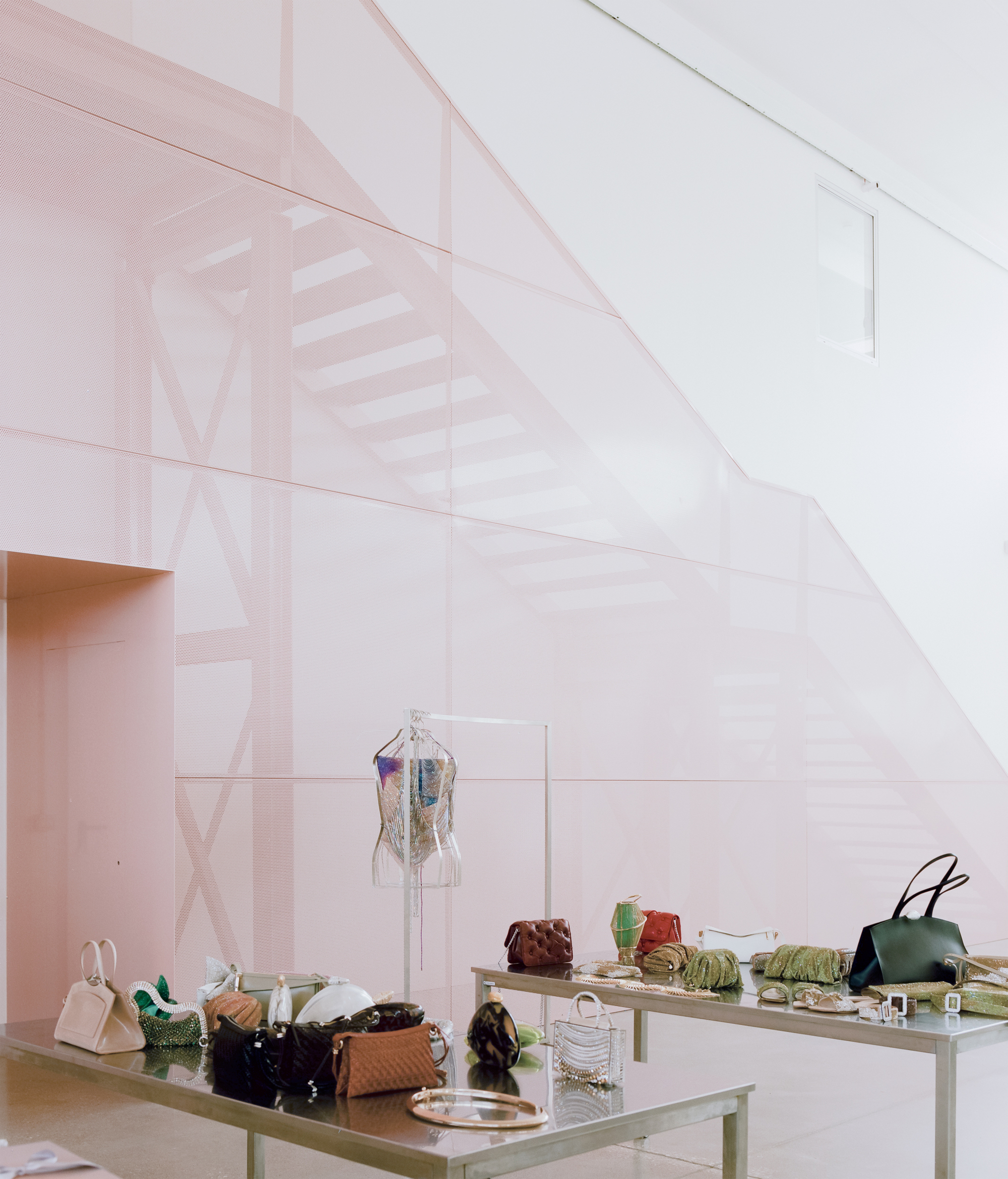 Translucent pink partition wall enclosing display tables with handbags and garments beneath a sloping ceiling