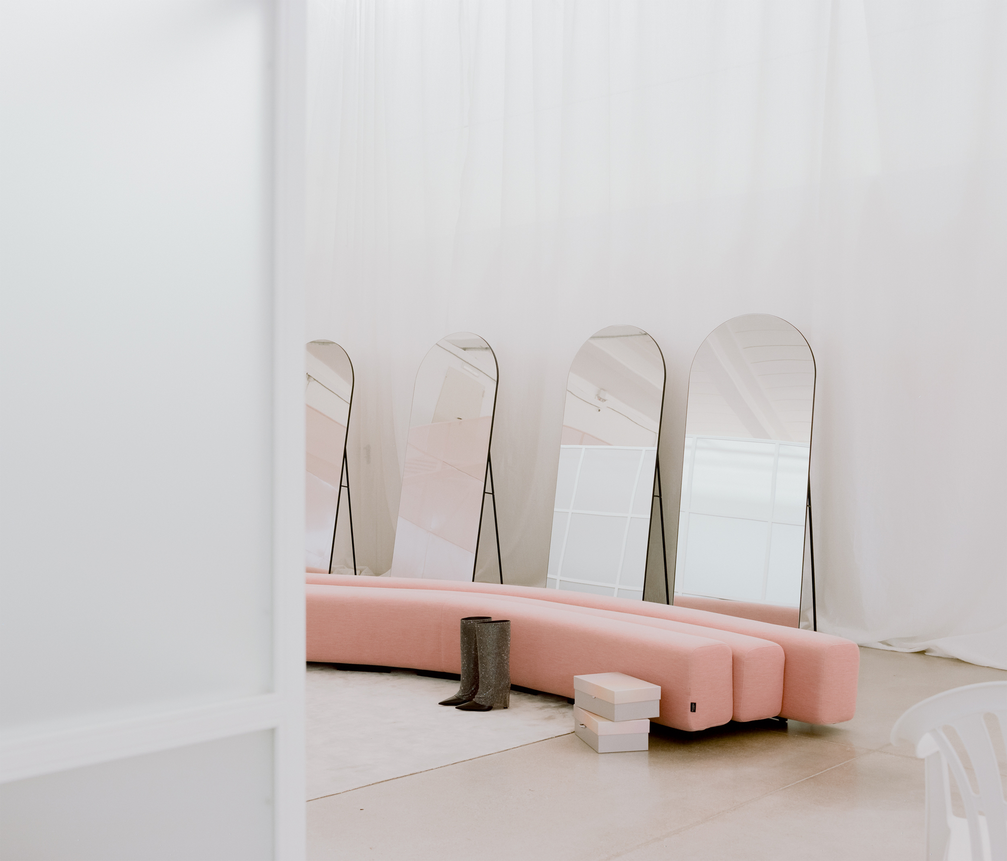 Pink upholstered seating base with arched mirrors leaning against the white wall