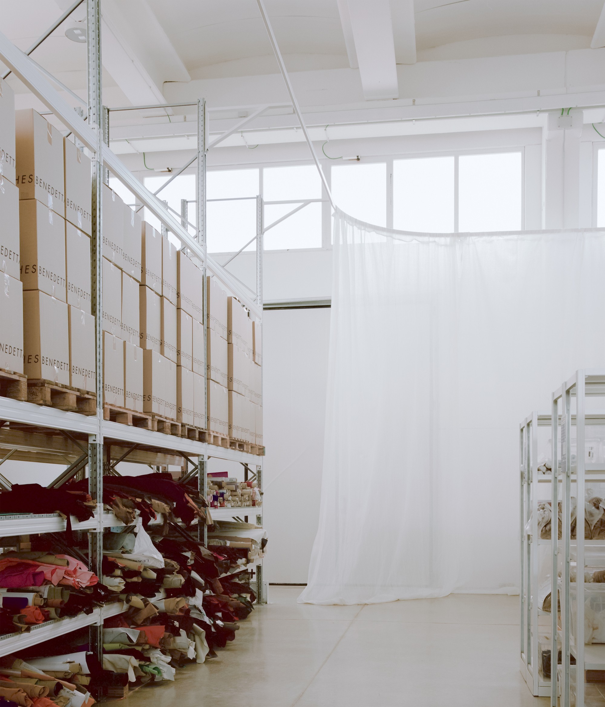 Workshop interior with metal shelving holding fabric bolts and a curved white curtain partition