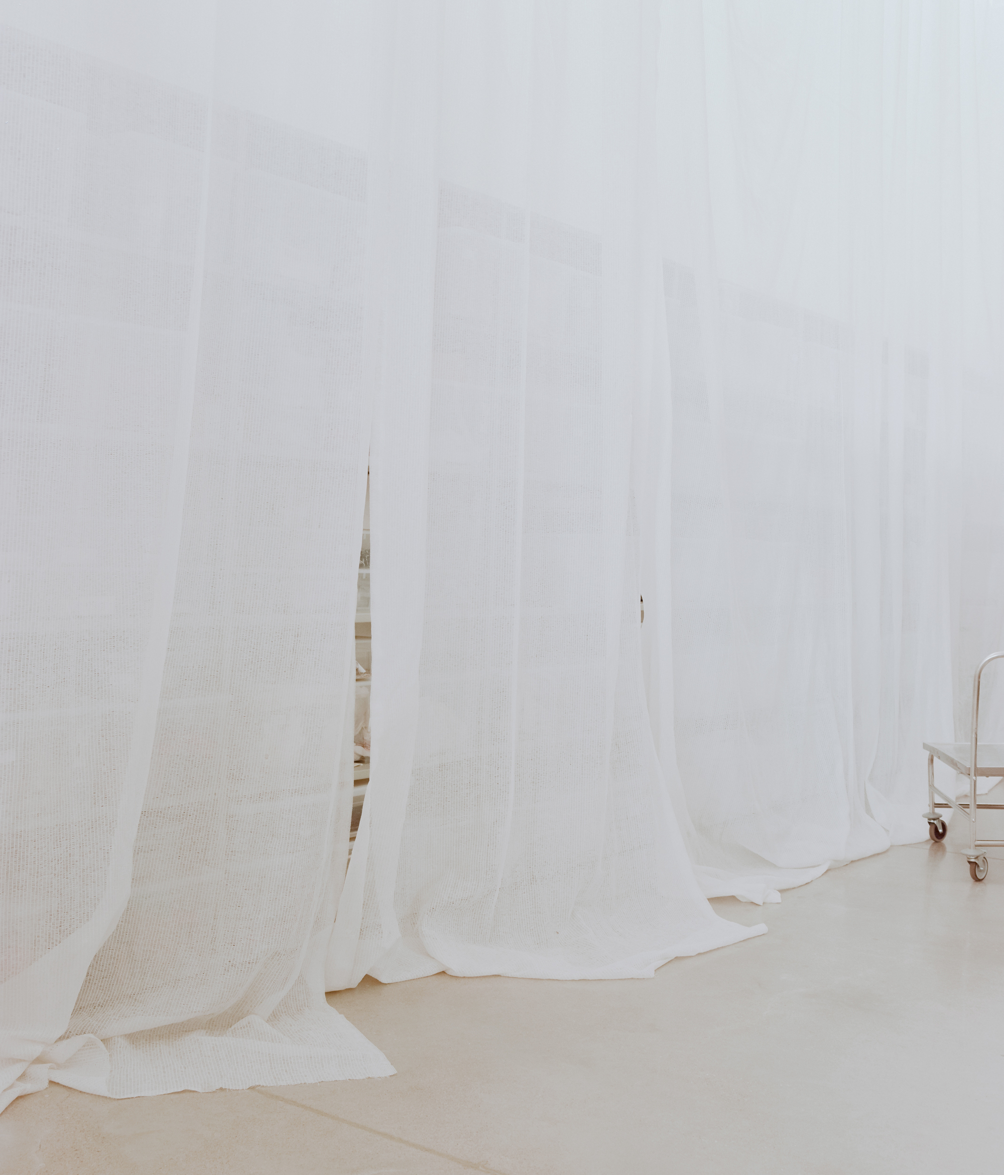 Floor-to-ceiling white mesh curtains hanging in soft folds across the workroom