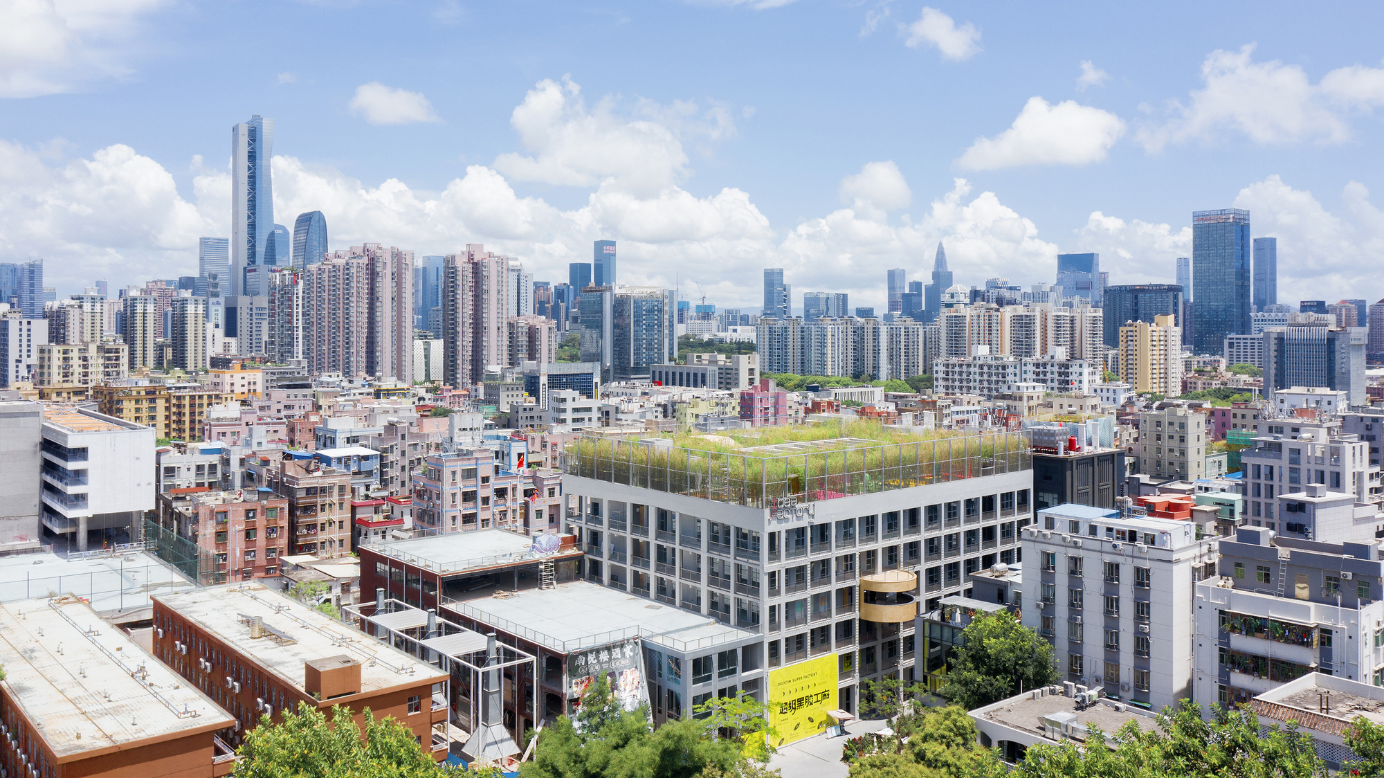 Rooftop green field on a rectangular building surrounded by dense urban fabric under scattered clouds