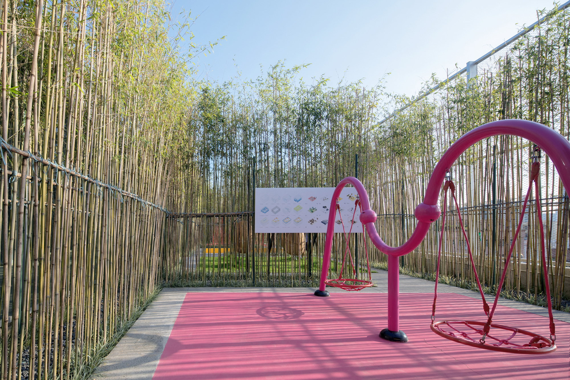 Pink rubberized play area with magenta climbing sculpture backed by bamboo grove and tall bamboo stalks