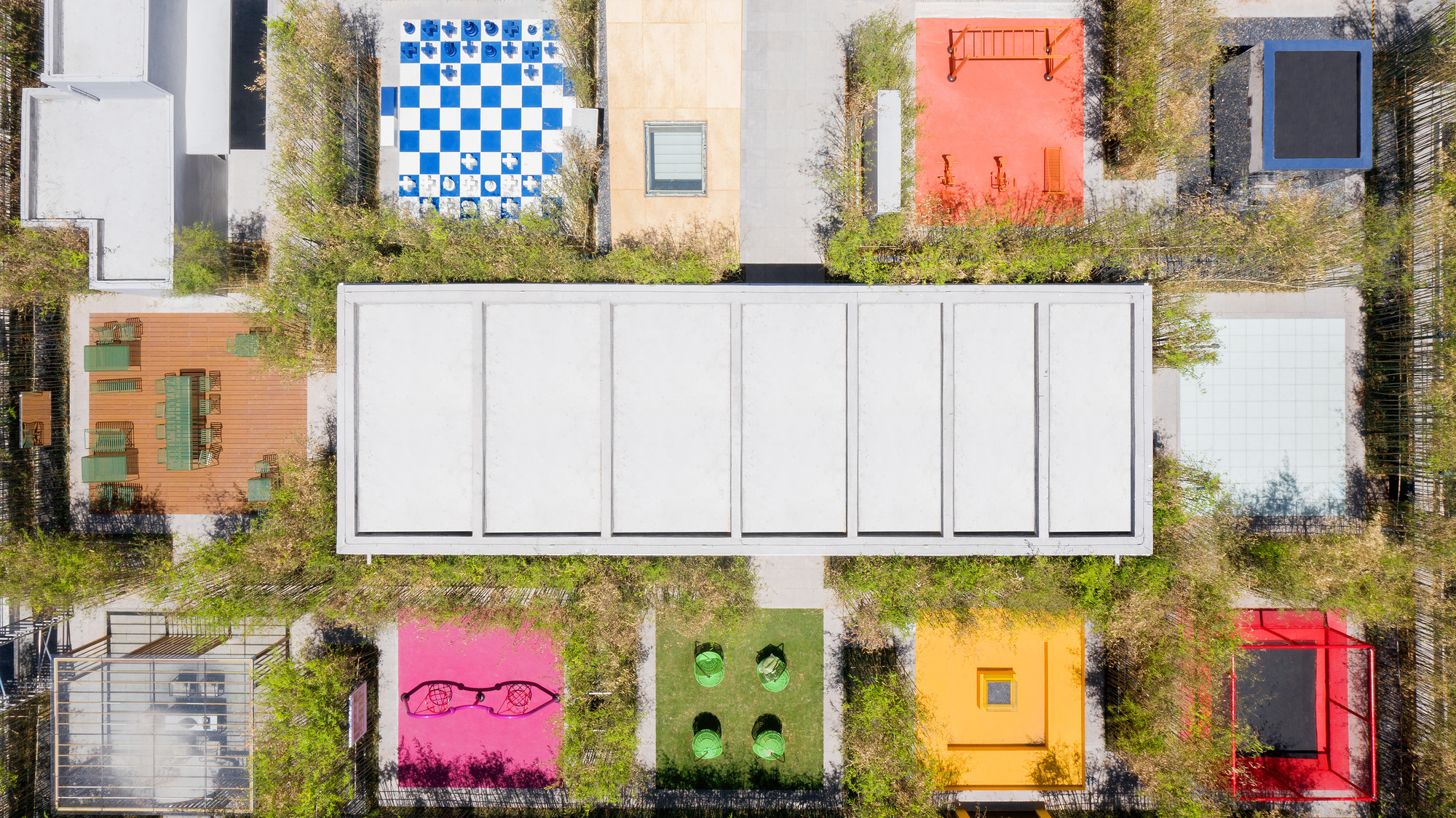 Drone view of the white skylight bar flanked by planted terraces and colored tile courts in autumn grasses