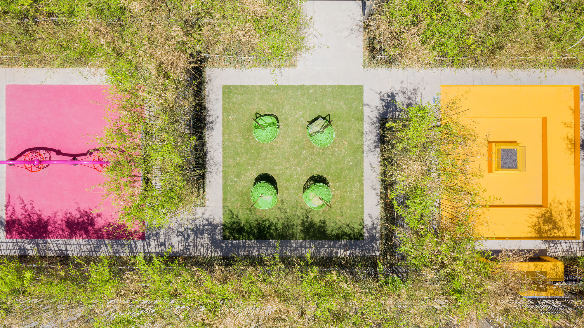 Top-down view of three tiled pavilions in pink, green, and yellow surrounded by overgrown vegetation