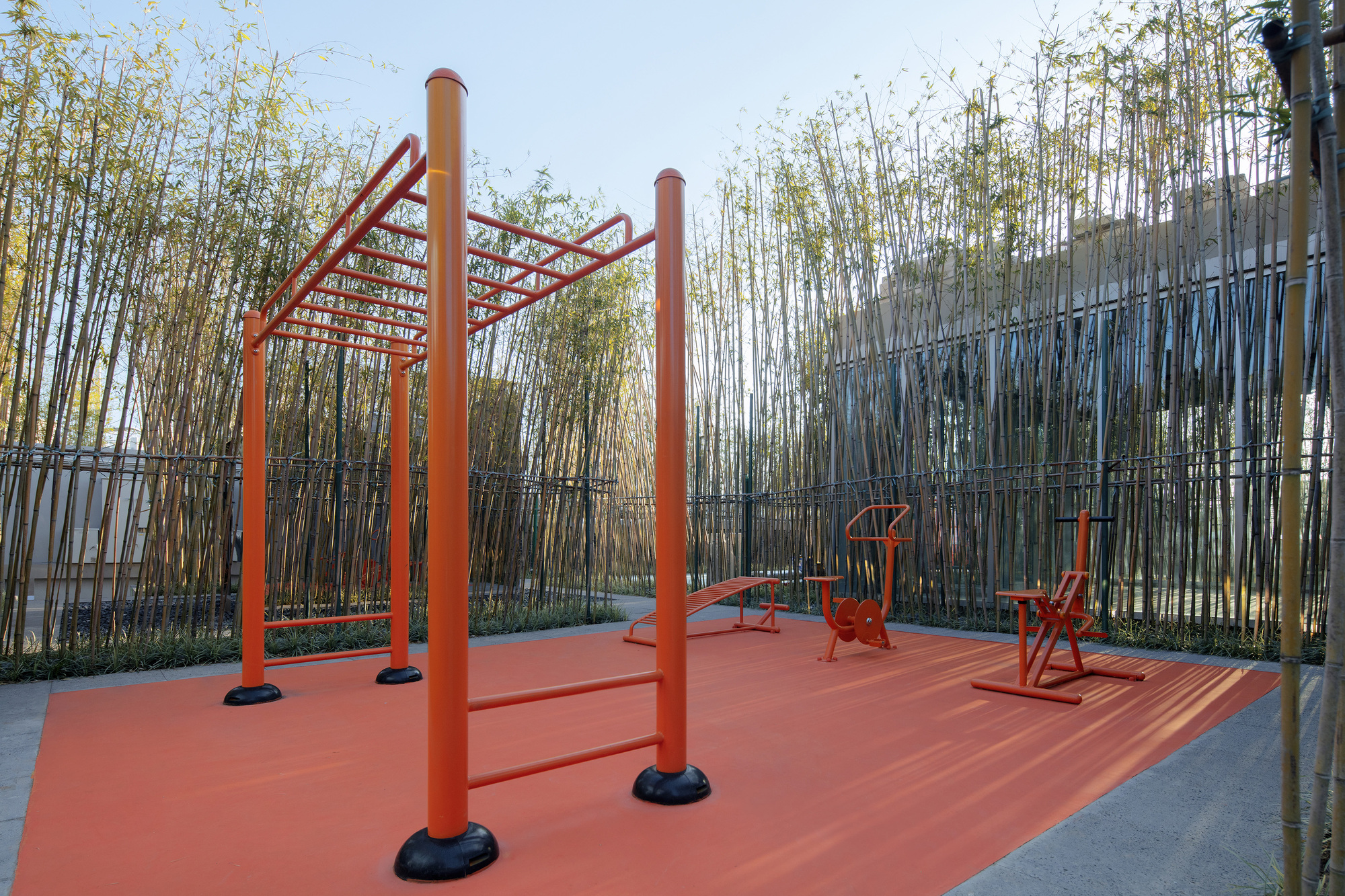 Orange outdoor exercise area with metal equipment on a rubber surface enclosed by bamboo screens