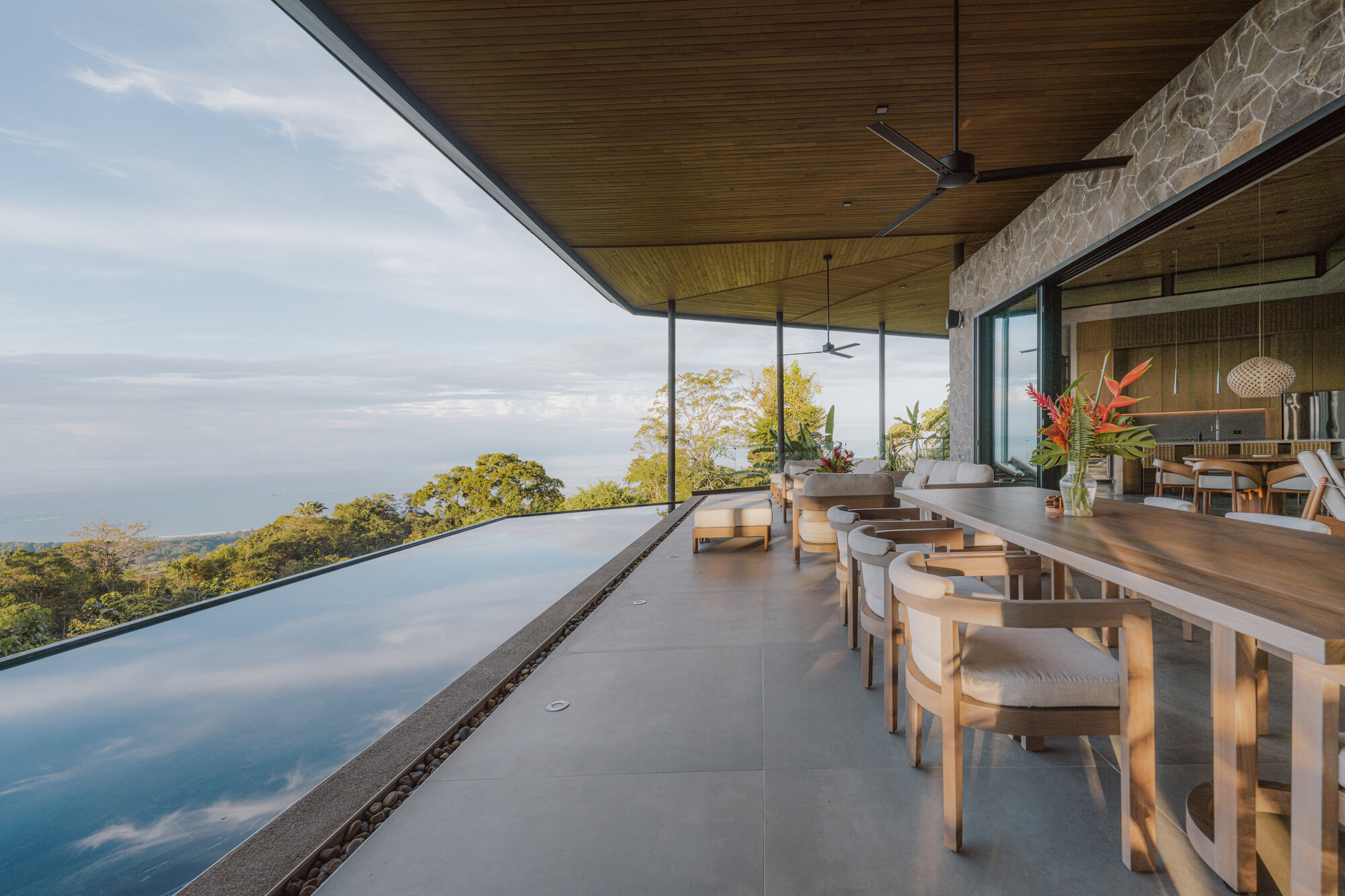 Covered terrace with infinity pool edge and timber ceiling overlooking the valley below