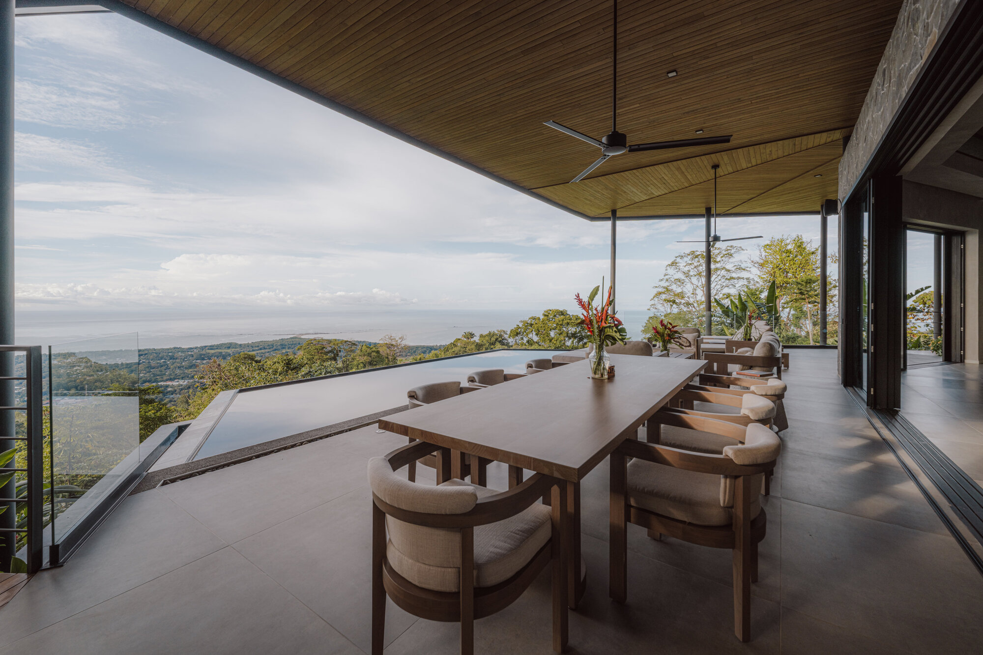 Dining terrace with timber ceiling and table overlooking valley and distant coastline