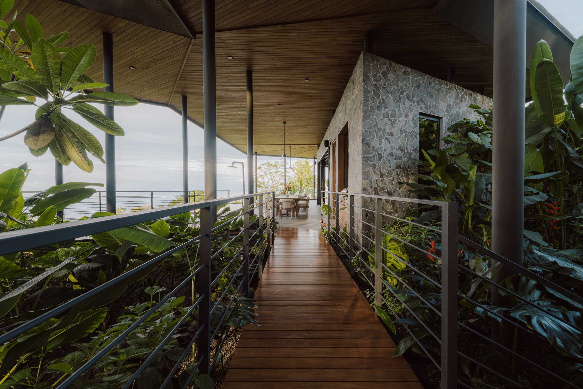 Timber bridge with metal railings flanked by tropical plantings leading to stone wall volume