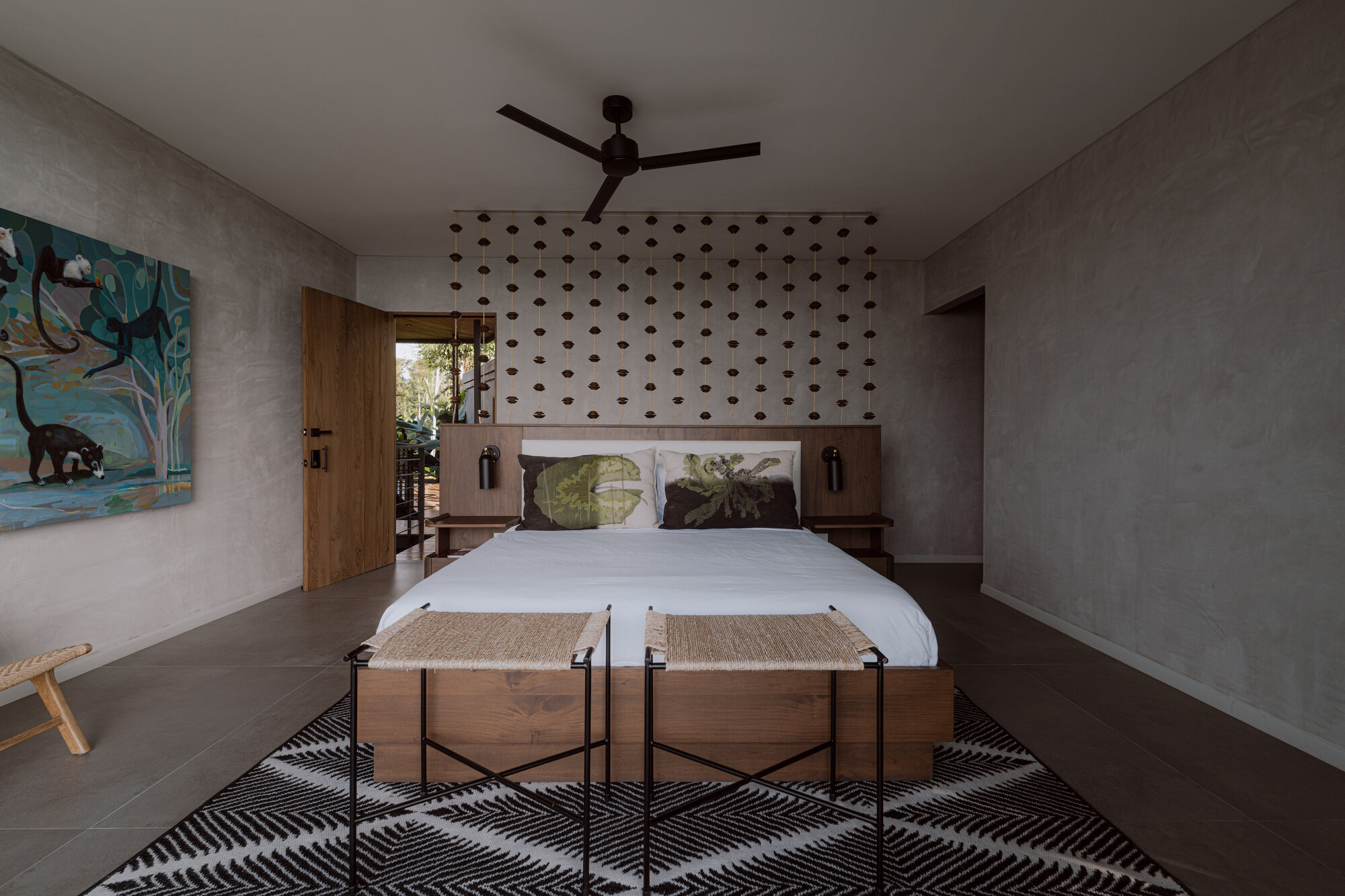 Bedroom with perforated concrete headboard wall, timber door, and polished concrete floor