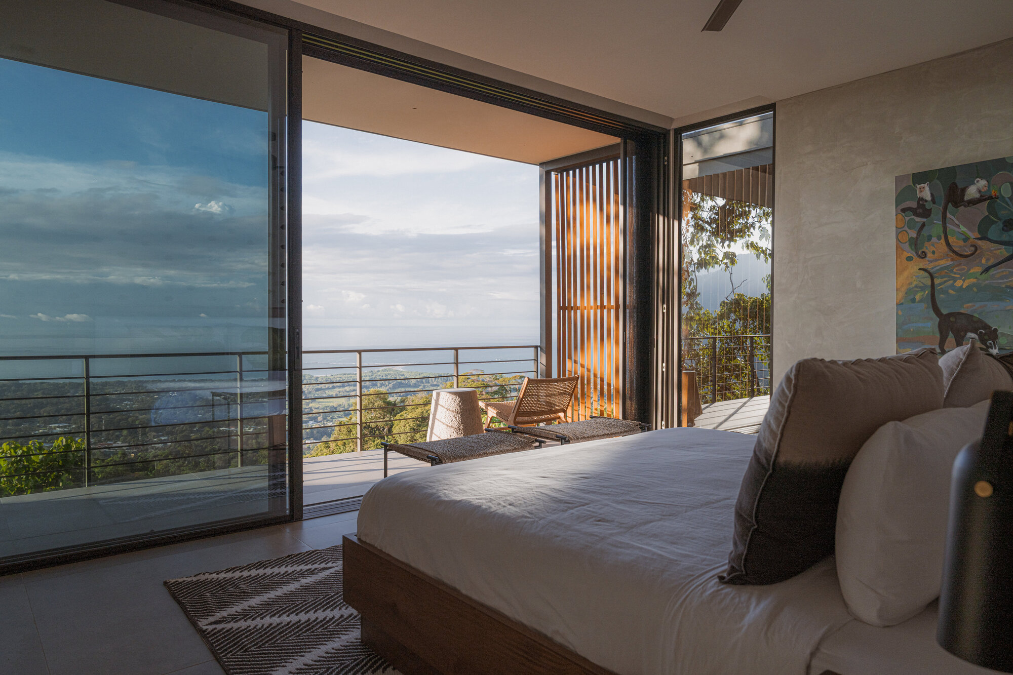 Bedroom opening to balcony with timber louvers and distant valley view at sunset