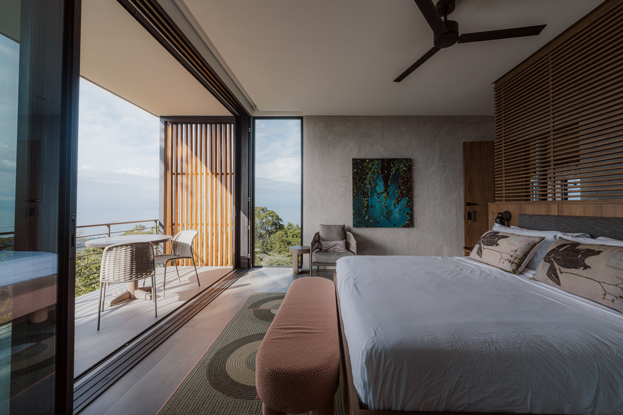 Bedroom with floor-to-ceiling glass doors opening to a terrace overlooking forested hills