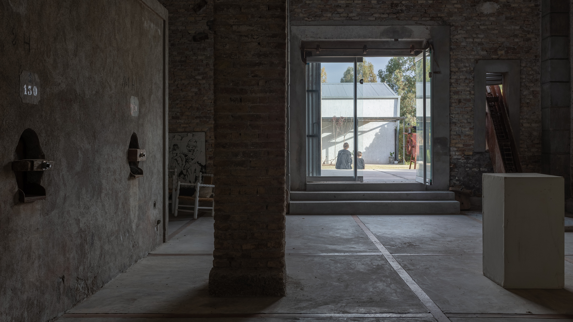 Interior gallery space with exposed brick columns and view through glazed opening to courtyard beyond
