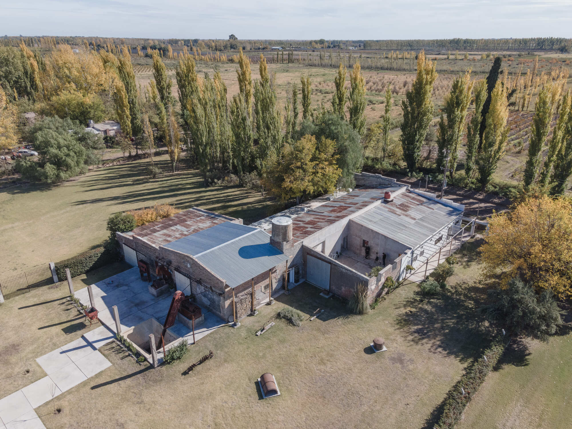 Aerial view of the compound with corrugated metal roofs surrounded by tall poplars in autumn light