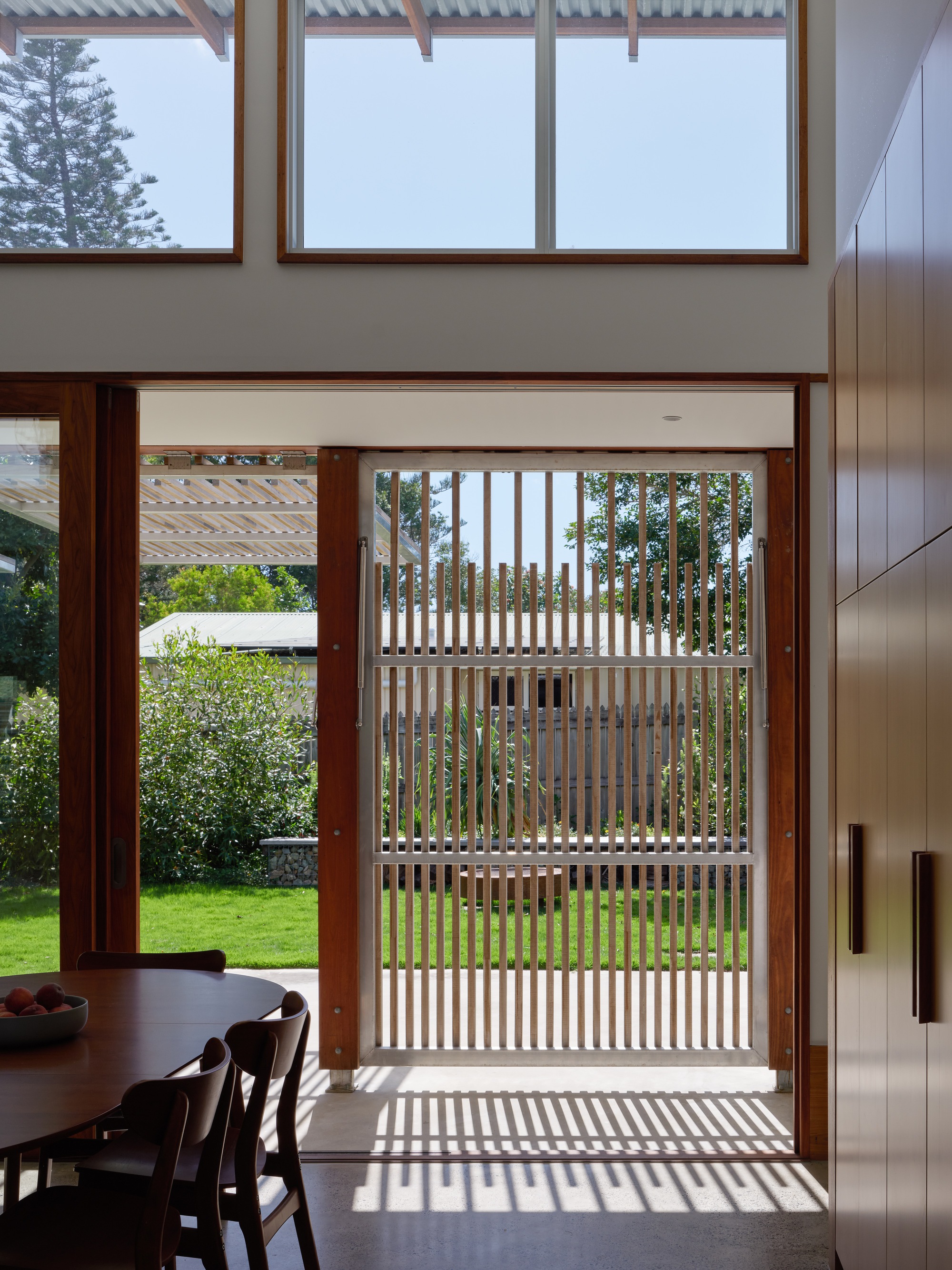 Interior view through open timber screen door casting striped shadows across the polished concrete floor
