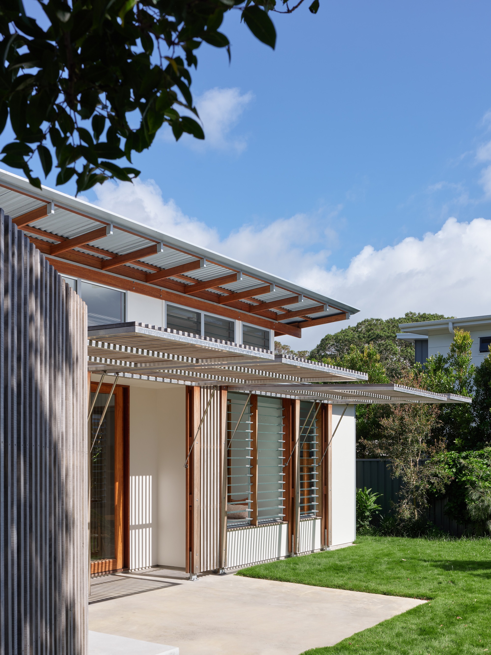 Exterior corner showing the cantilevered roof with exposed timber rafters and folding screen panels beneath overhanging foliage