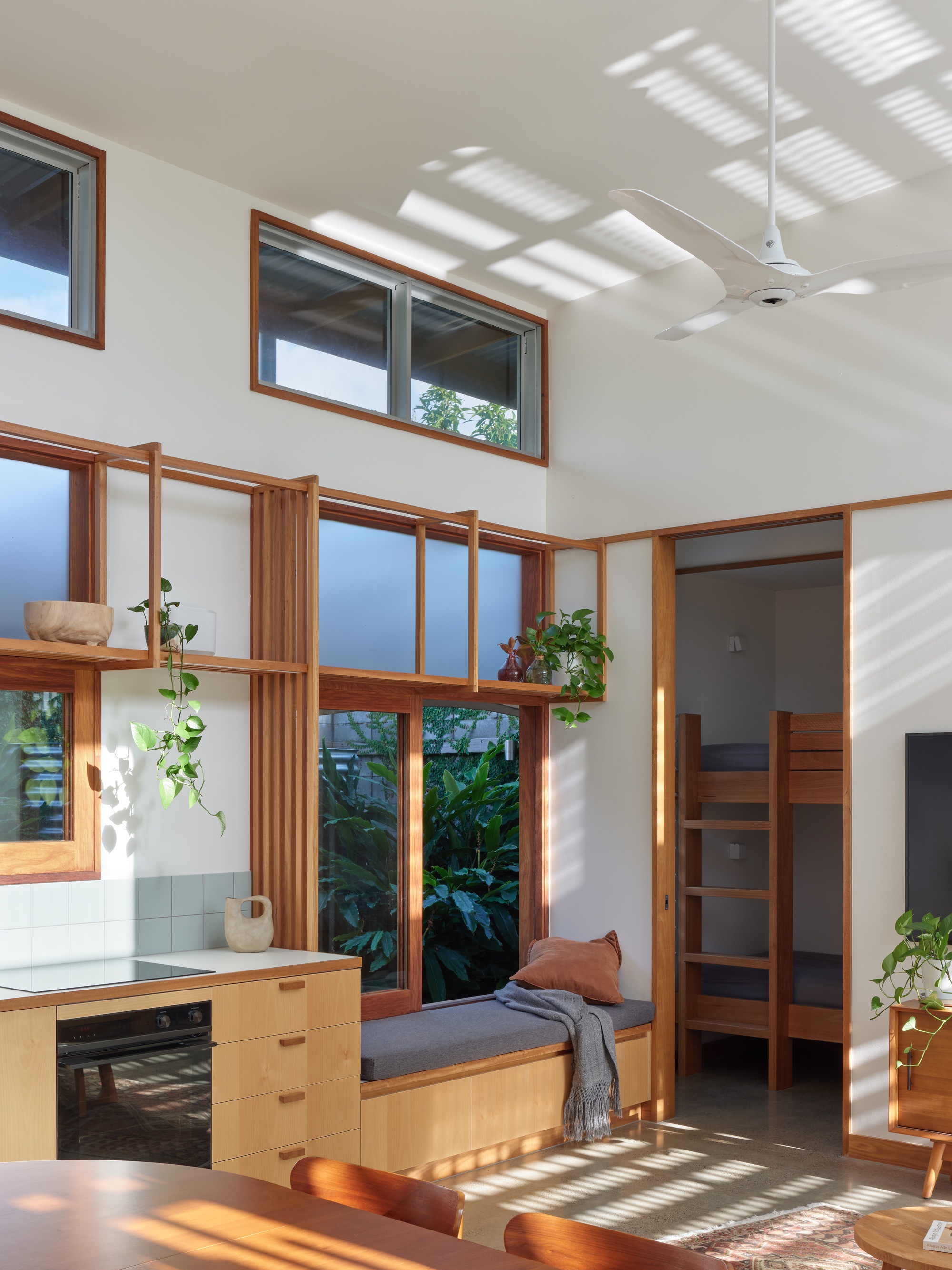 Interior living space with timber-framed windows casting striped shadows across white walls and built-in seating