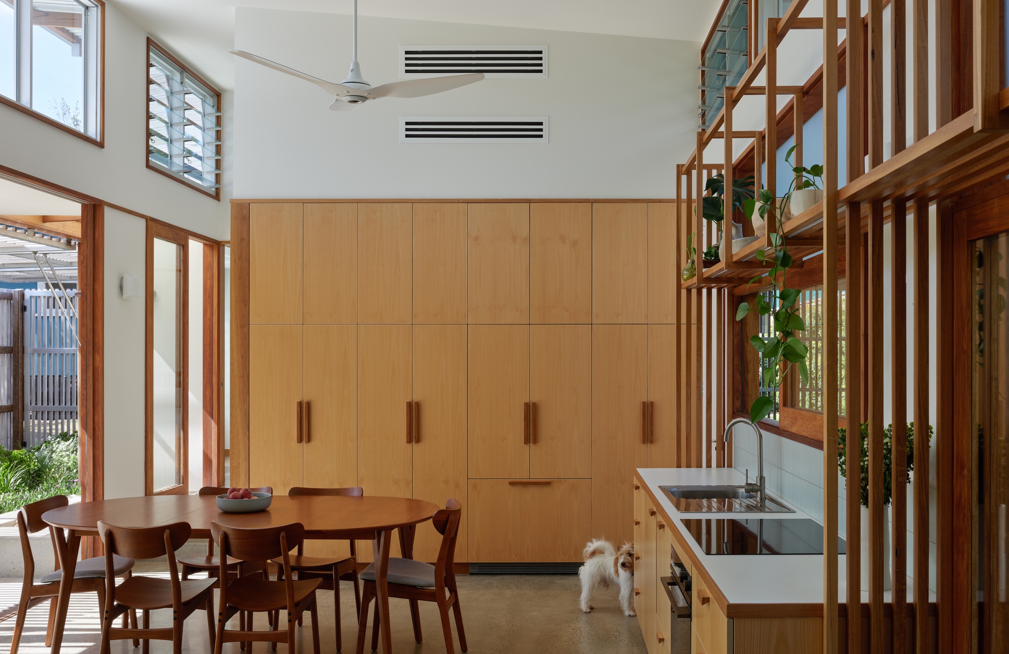 Open-plan dining area with timber cabinetry, timber staircase divider, and small dog on polished concrete