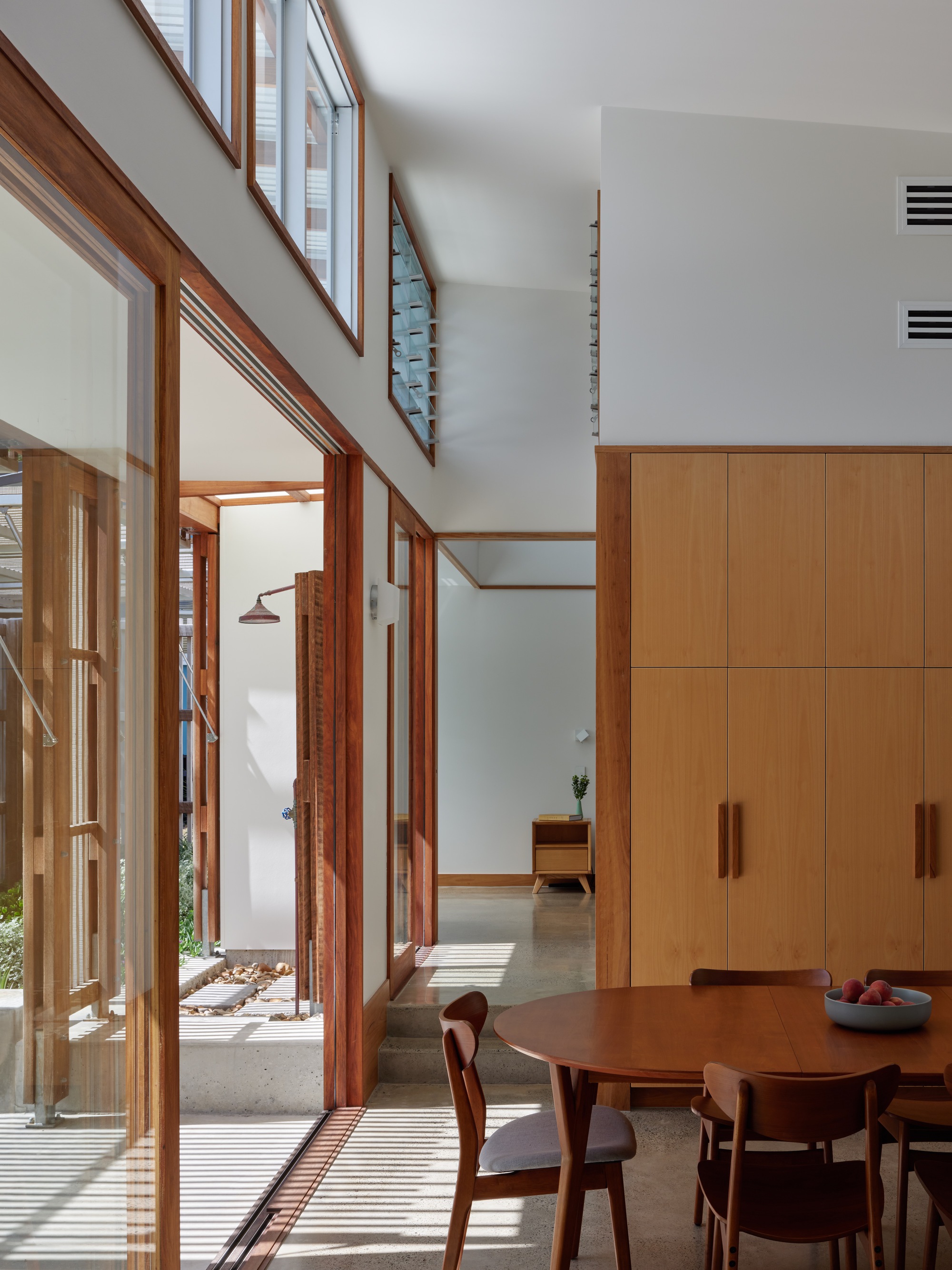 Interior view through glass doors to courtyard with striped shadow patterns on concrete floor